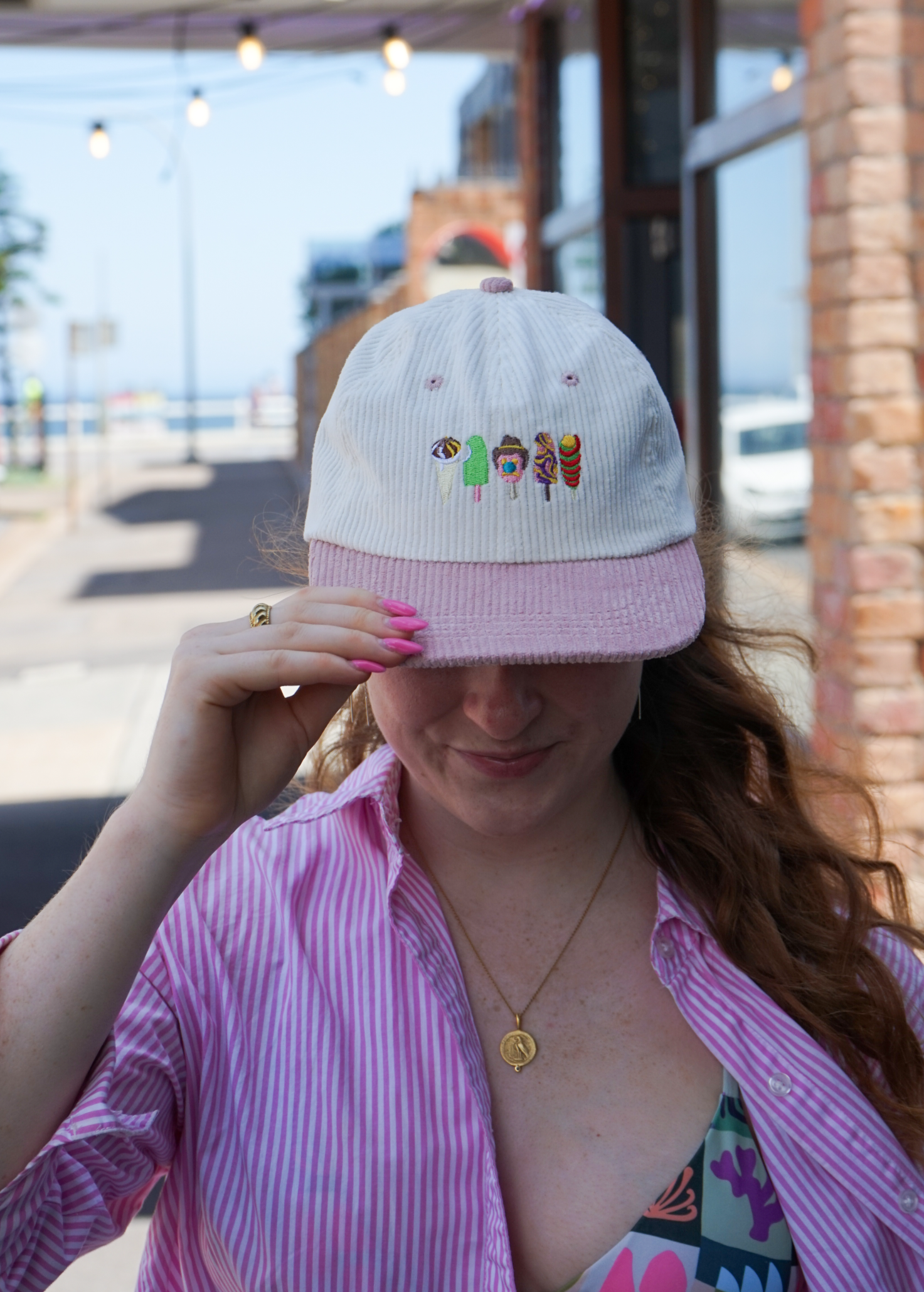 Person wearing a white cap with colorful text and a pink shirt outdoors.