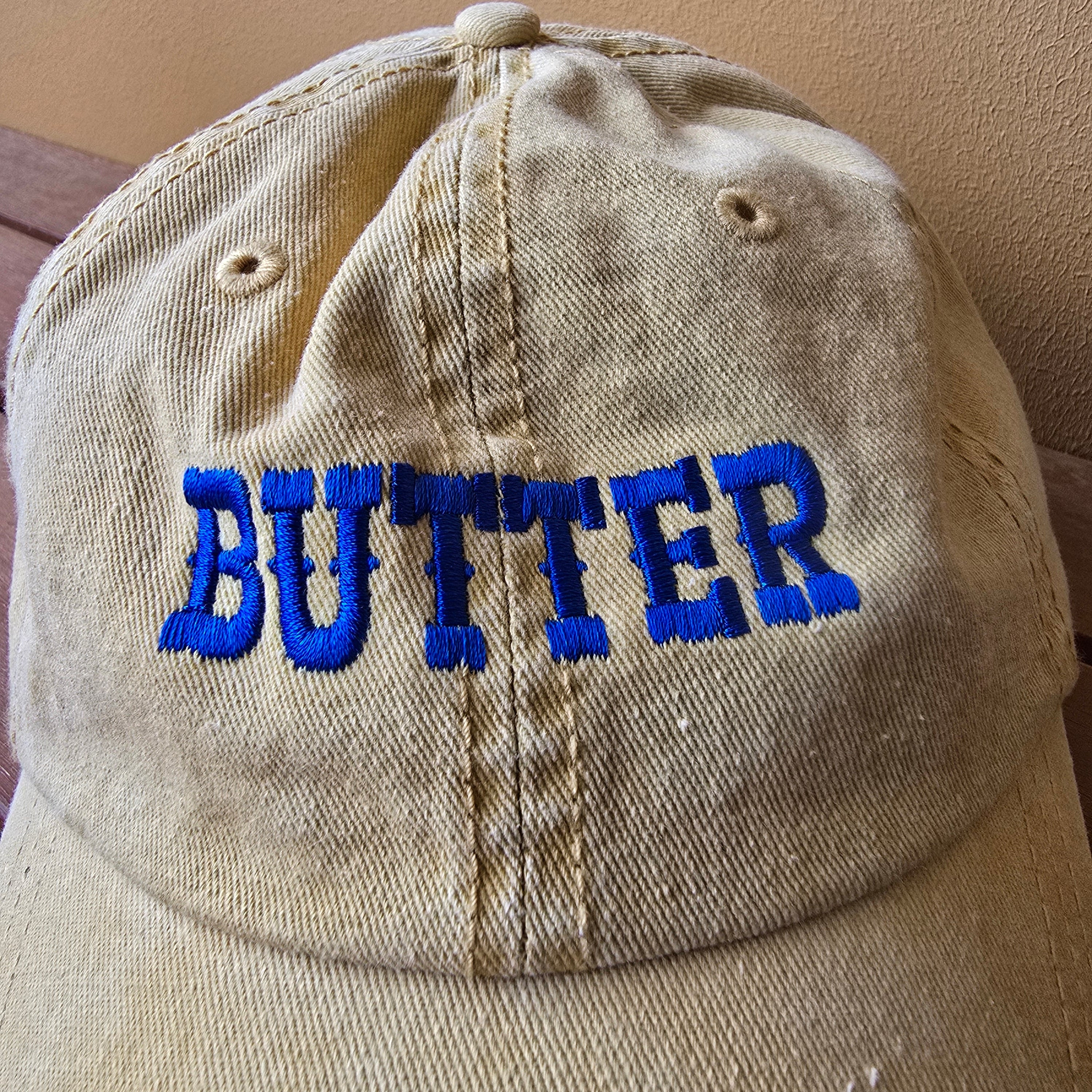 Beige cap with blue 'BUTTER' text on a beige background