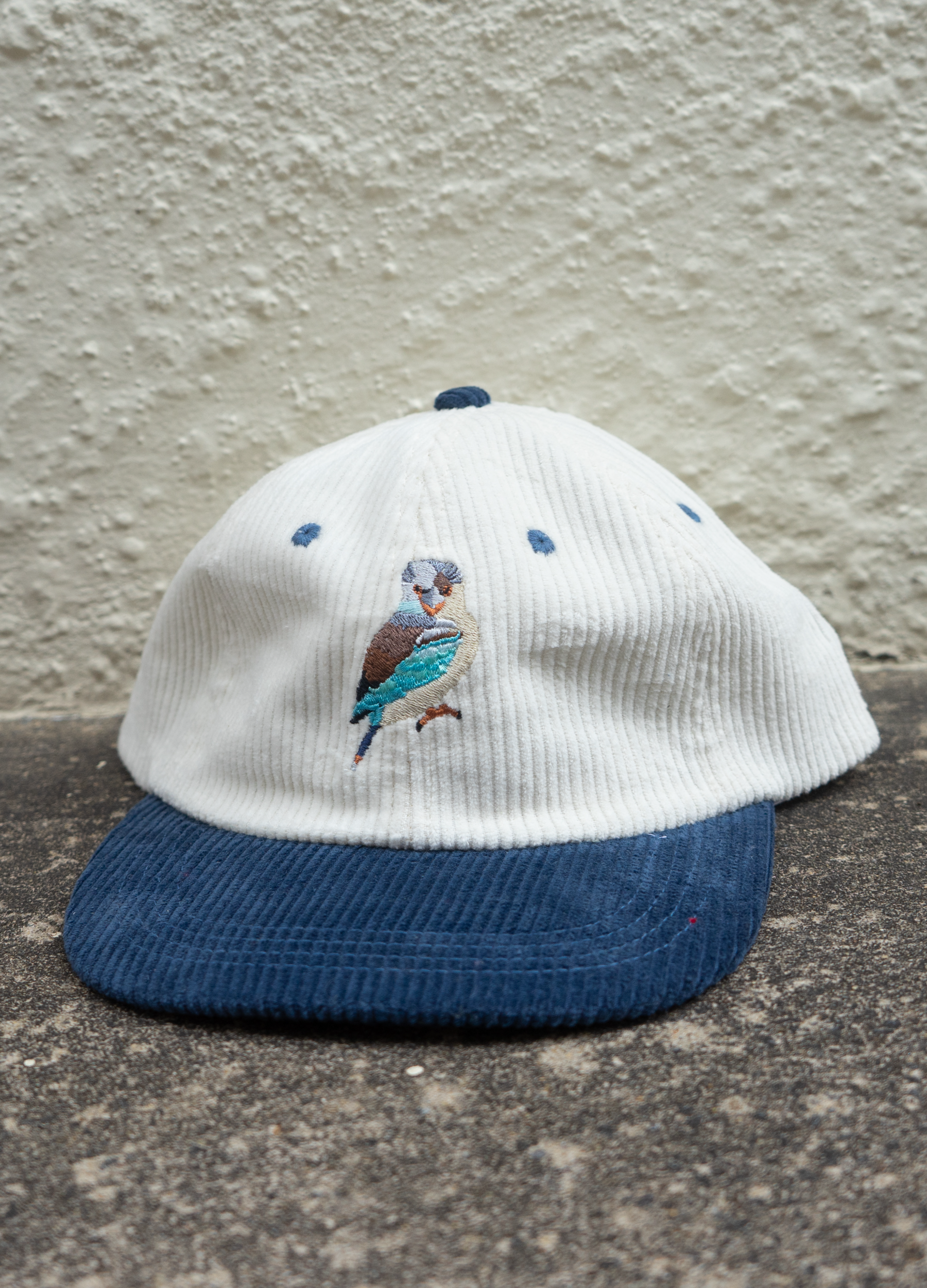 White cap with blue brim and embroidered bird design on a textured surface