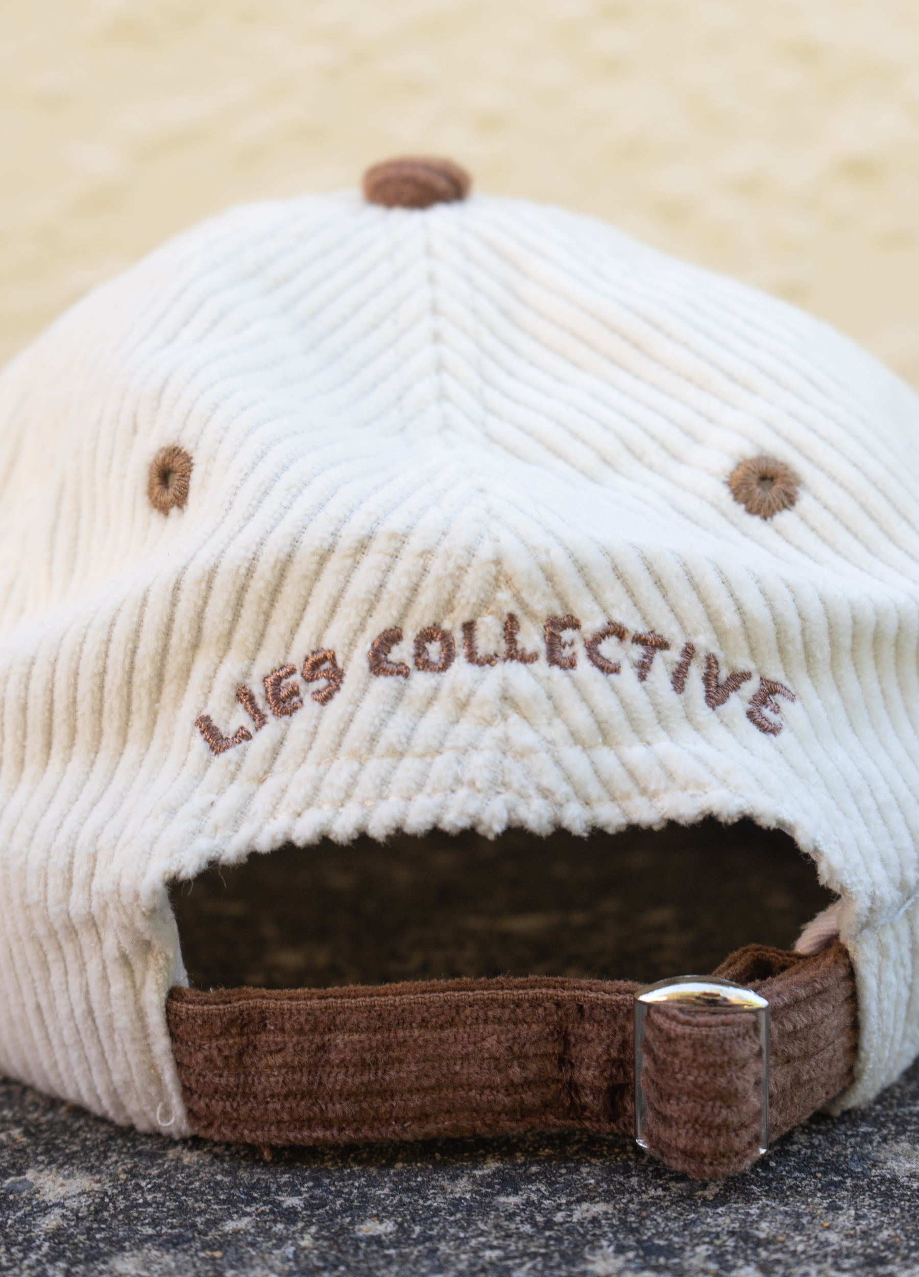 Beige cap with brown brim and embroidered text on a textured surface