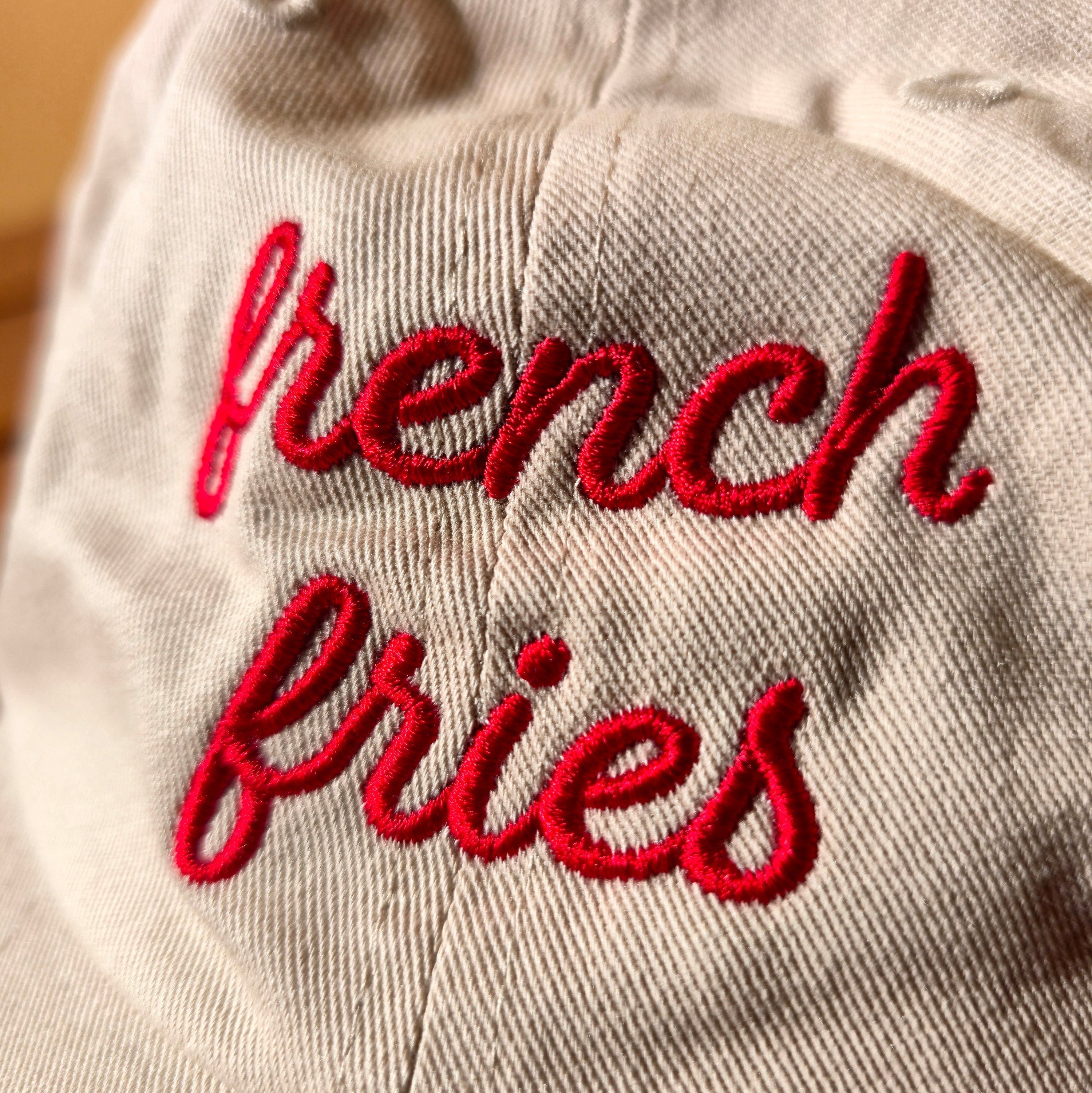 Text 'French fries' embroidered on a white hat with a blurred background