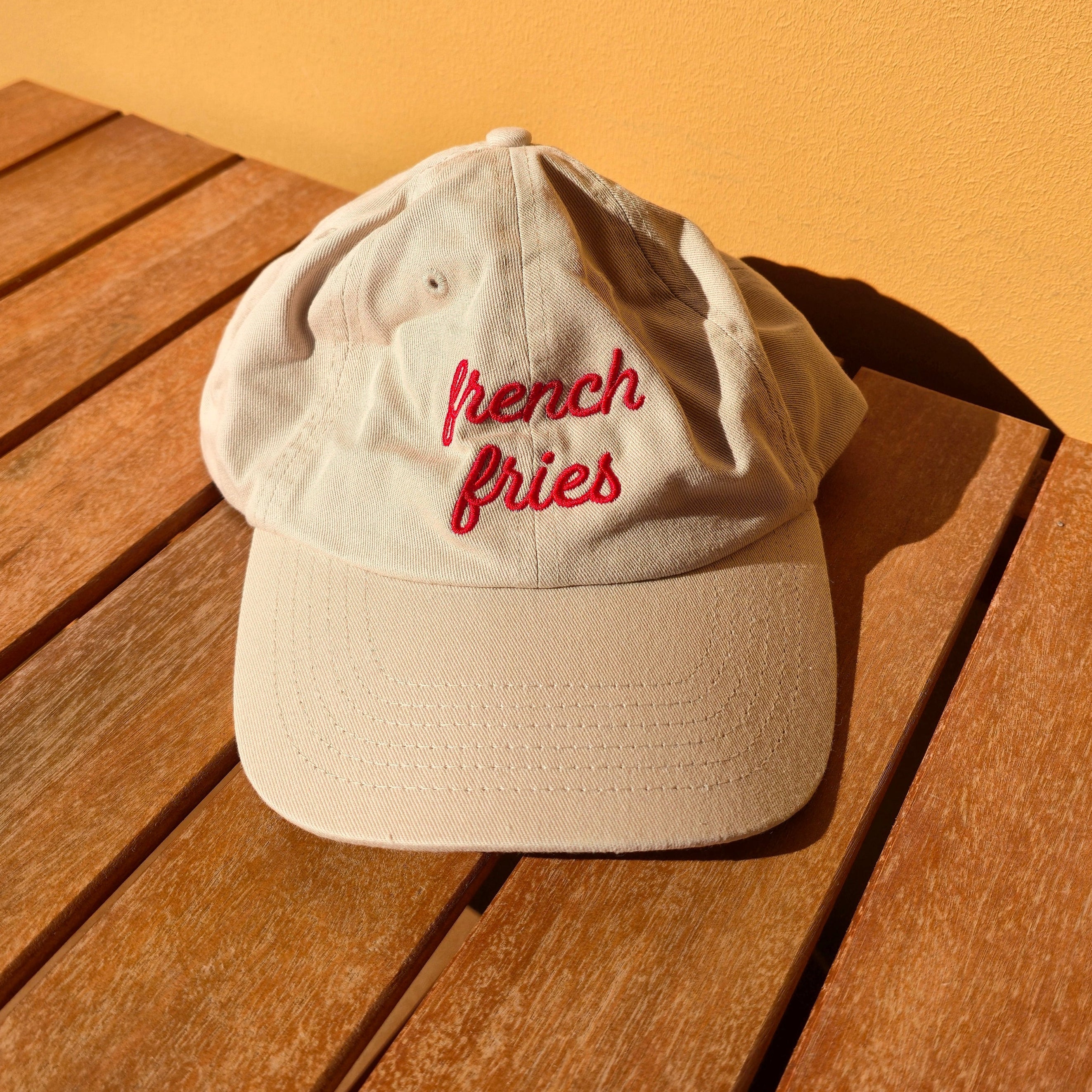 White cap with 'French Fries' text on a wooden surface with a yellowish-brown background