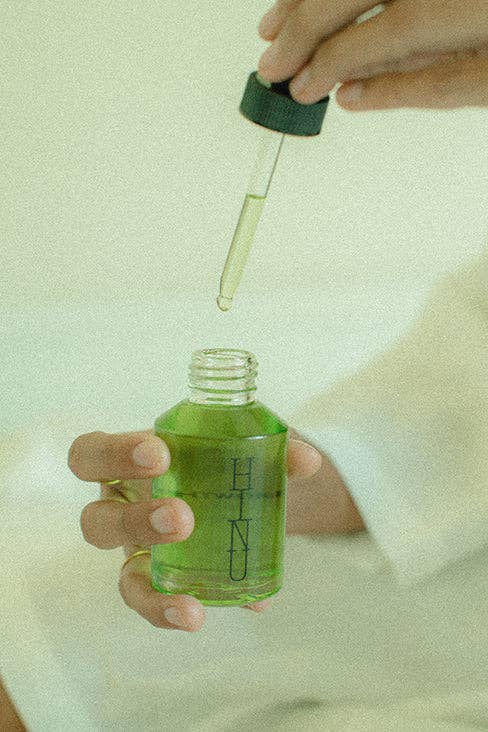 Person holding a bottle of green liquid with a dropper, against a light background