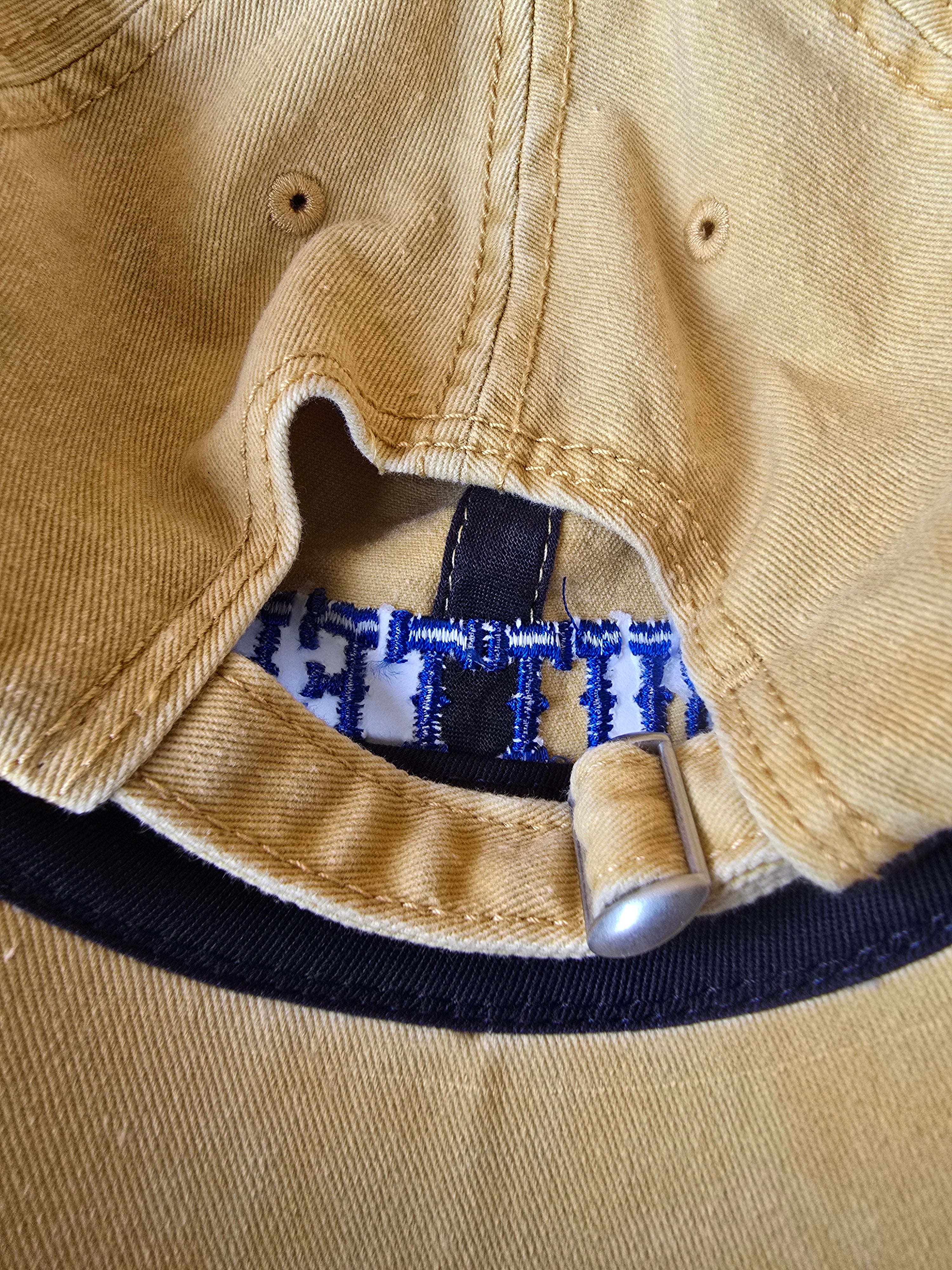 Close-up of a beige cap with a blue and white embroidered logo on a beige background