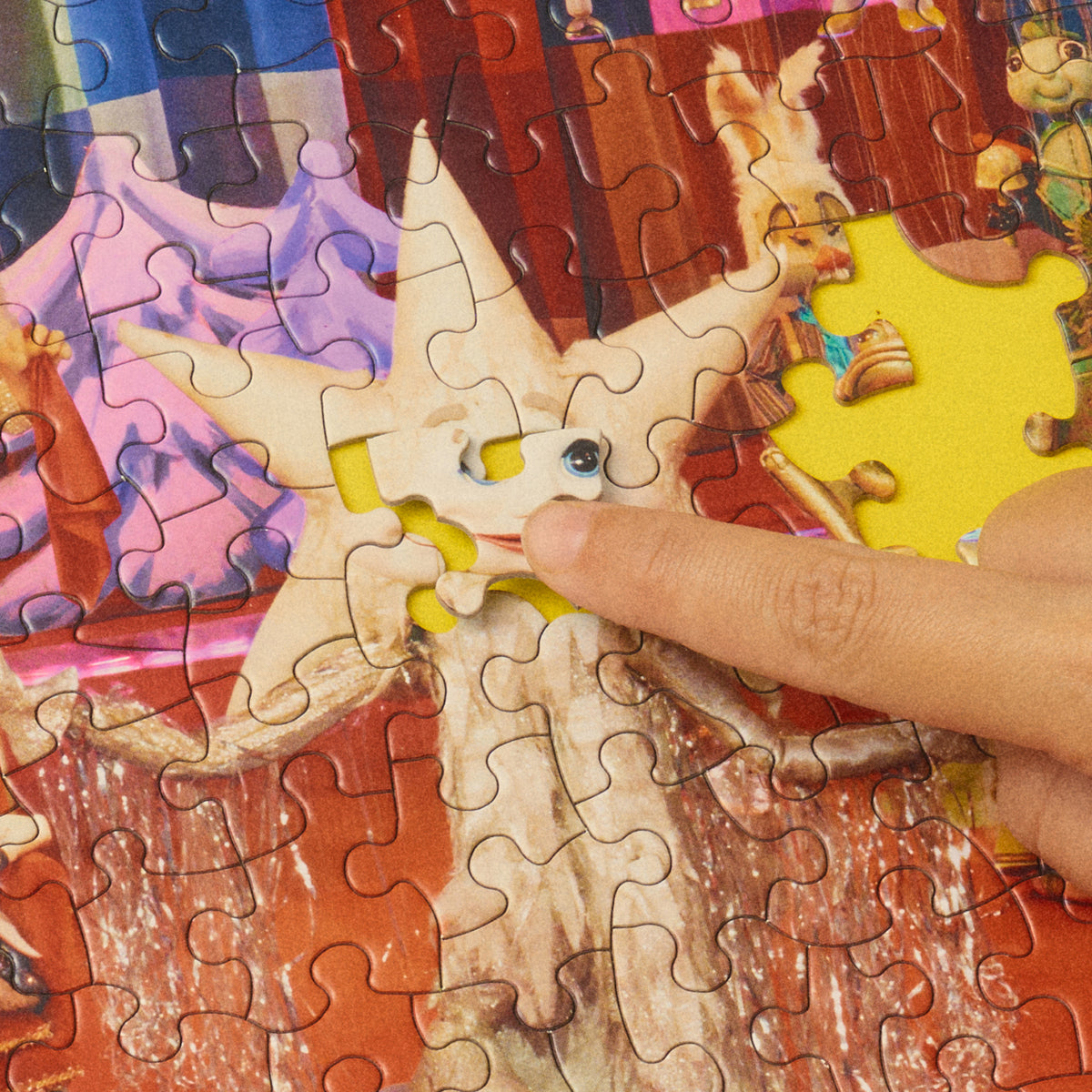 Finger pressing a piece into the silver star puppet’s face in the partially assembled On a Heartstring puzzle.