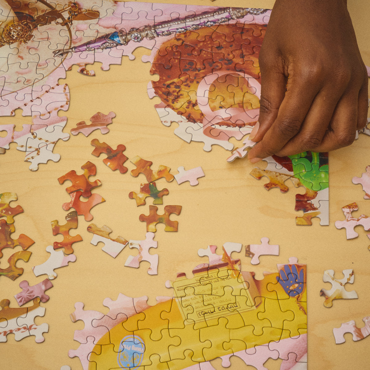Close-up of a hand placing a piece into the Jewish American Puzzle, with loose pieces on a wooden table.