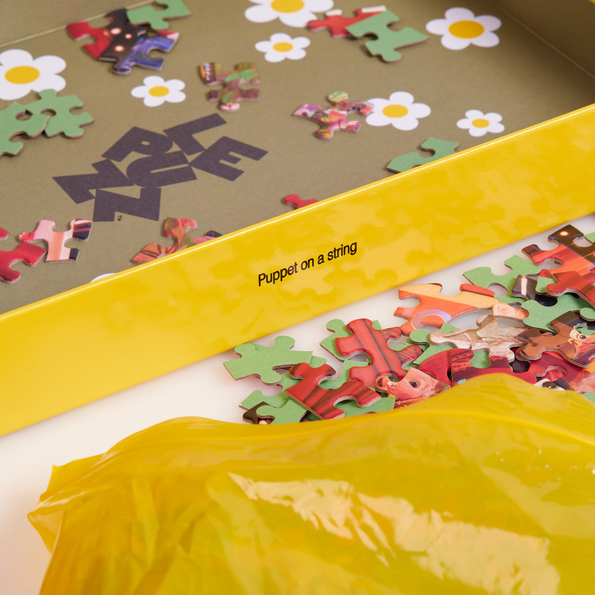 Loose On a Heartstring puzzle pieces beside a yellow bag and an open box decorated with white daisies.