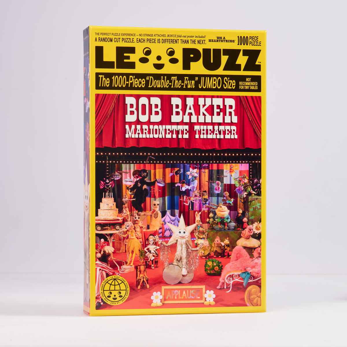 Le Puzz On a Heartstring 1000-piece puzzle box featuring colourful puppets beneath red theatre curtains.