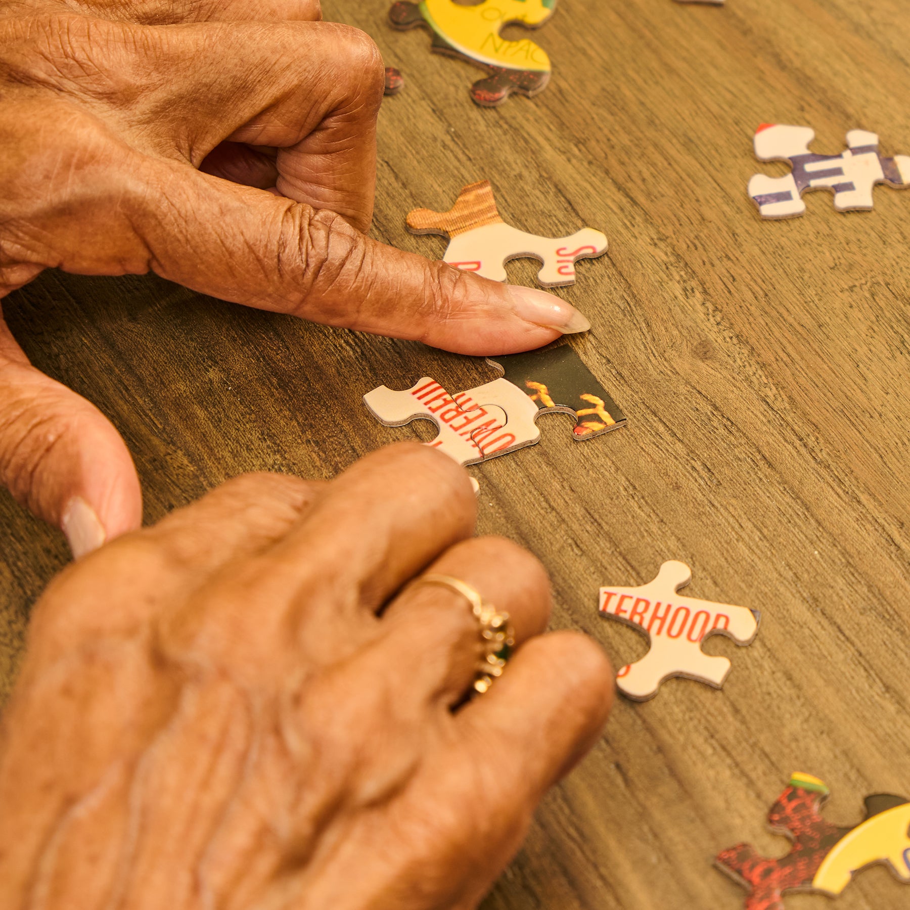 Close-up of hands working on a puzzle with pieces on a wooden surface