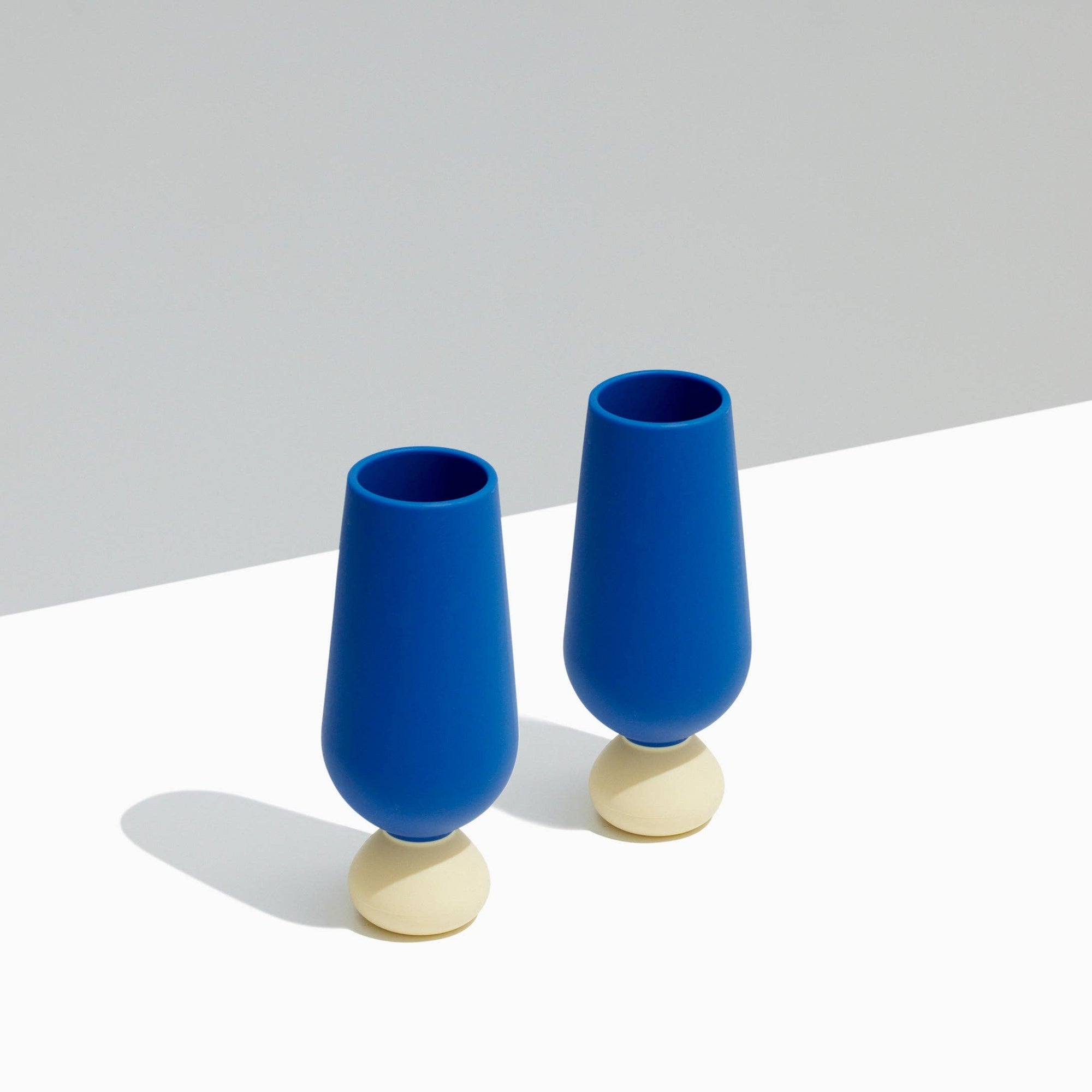 Two styld blue champagne siliscone cups with beige bases on a light gray background