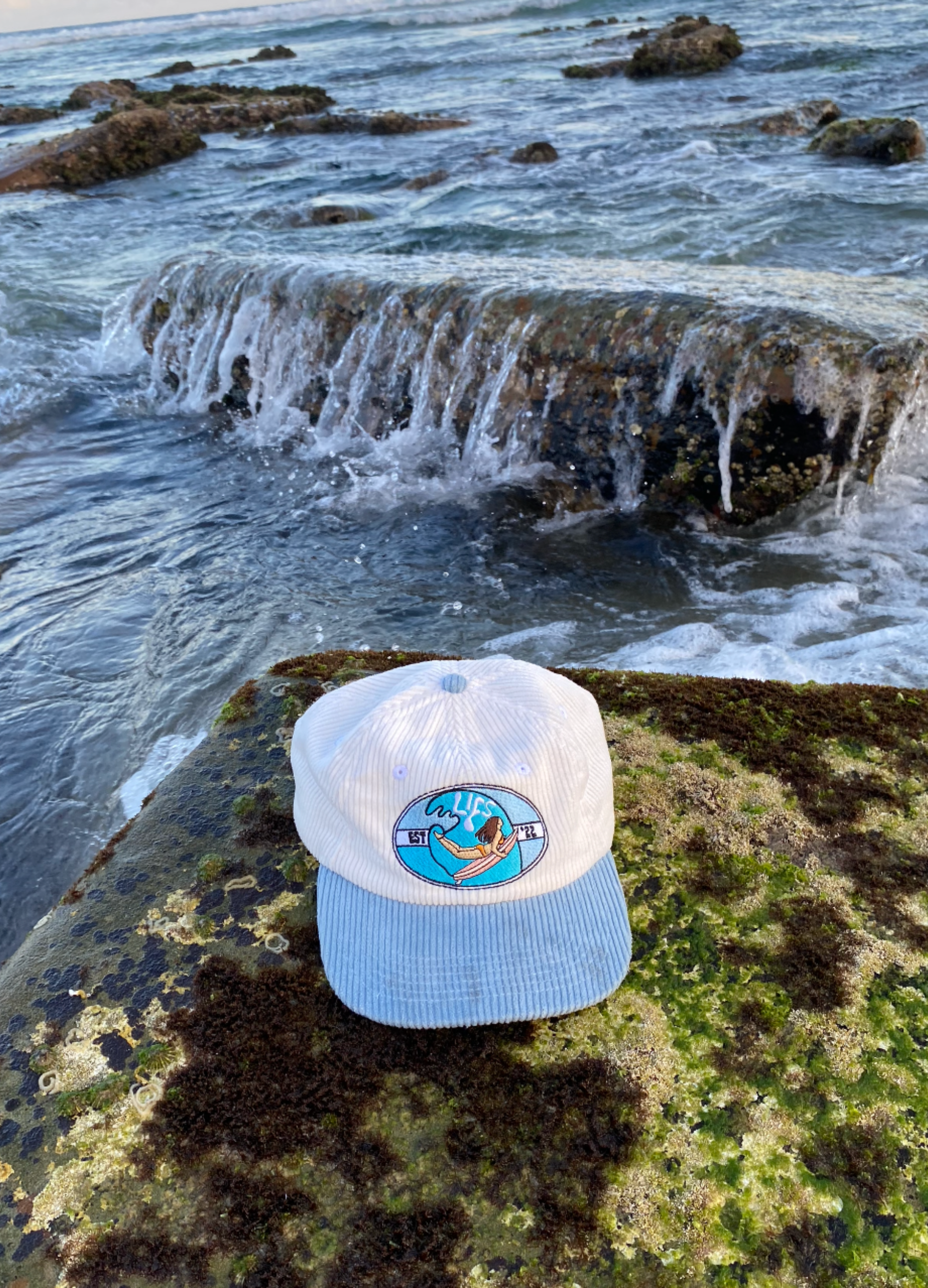 White cap with blue brim and logo on a rock by the ocean