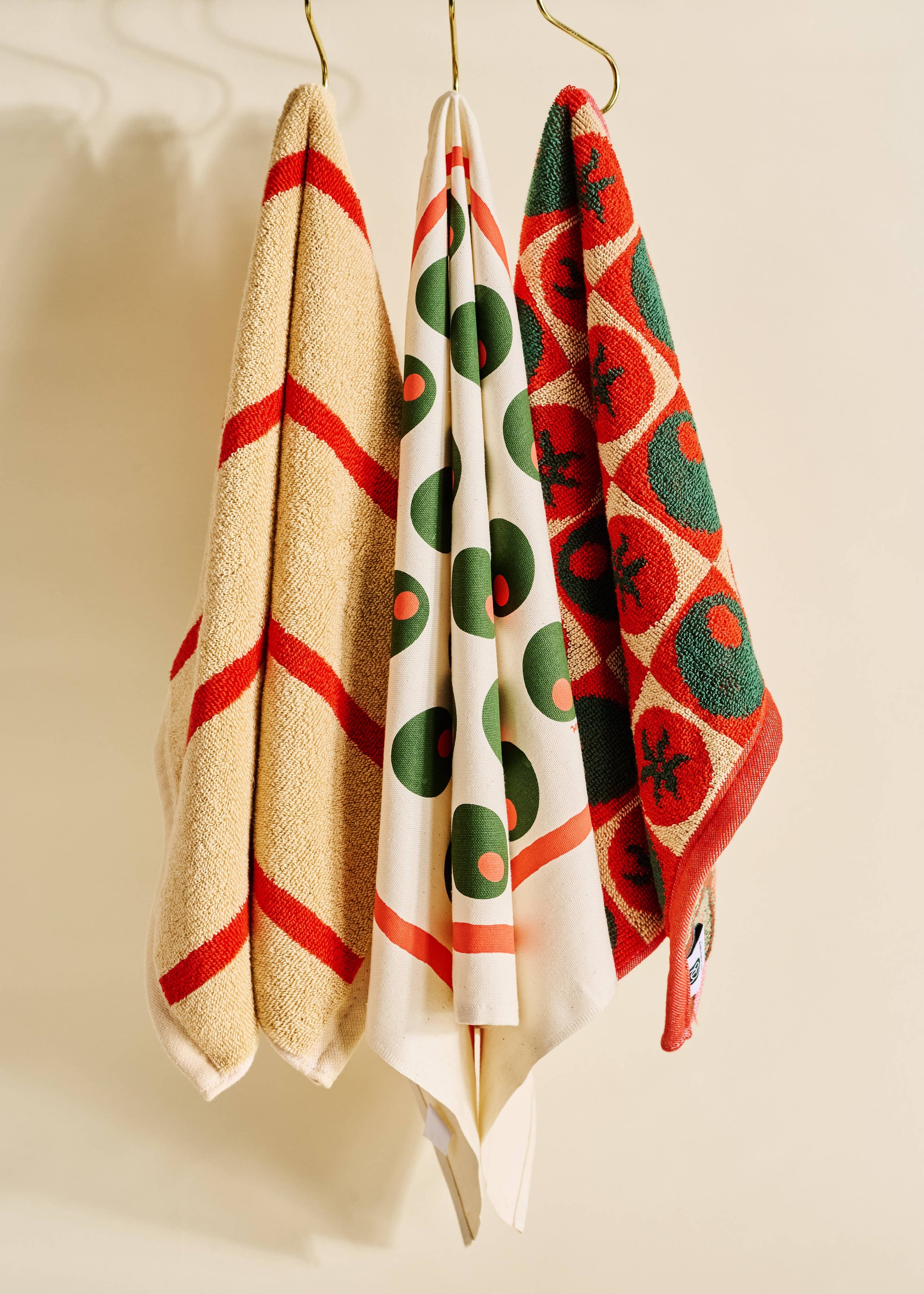 Three patterned towels hanging on a rack against a beige wall.