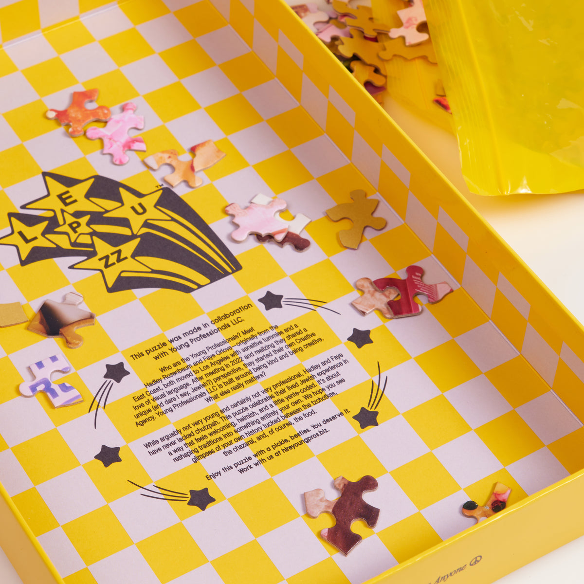Open yellow and white checkered box containing scattered jigsaw puzzle pieces, with printed instructions and branding on the inner lid.