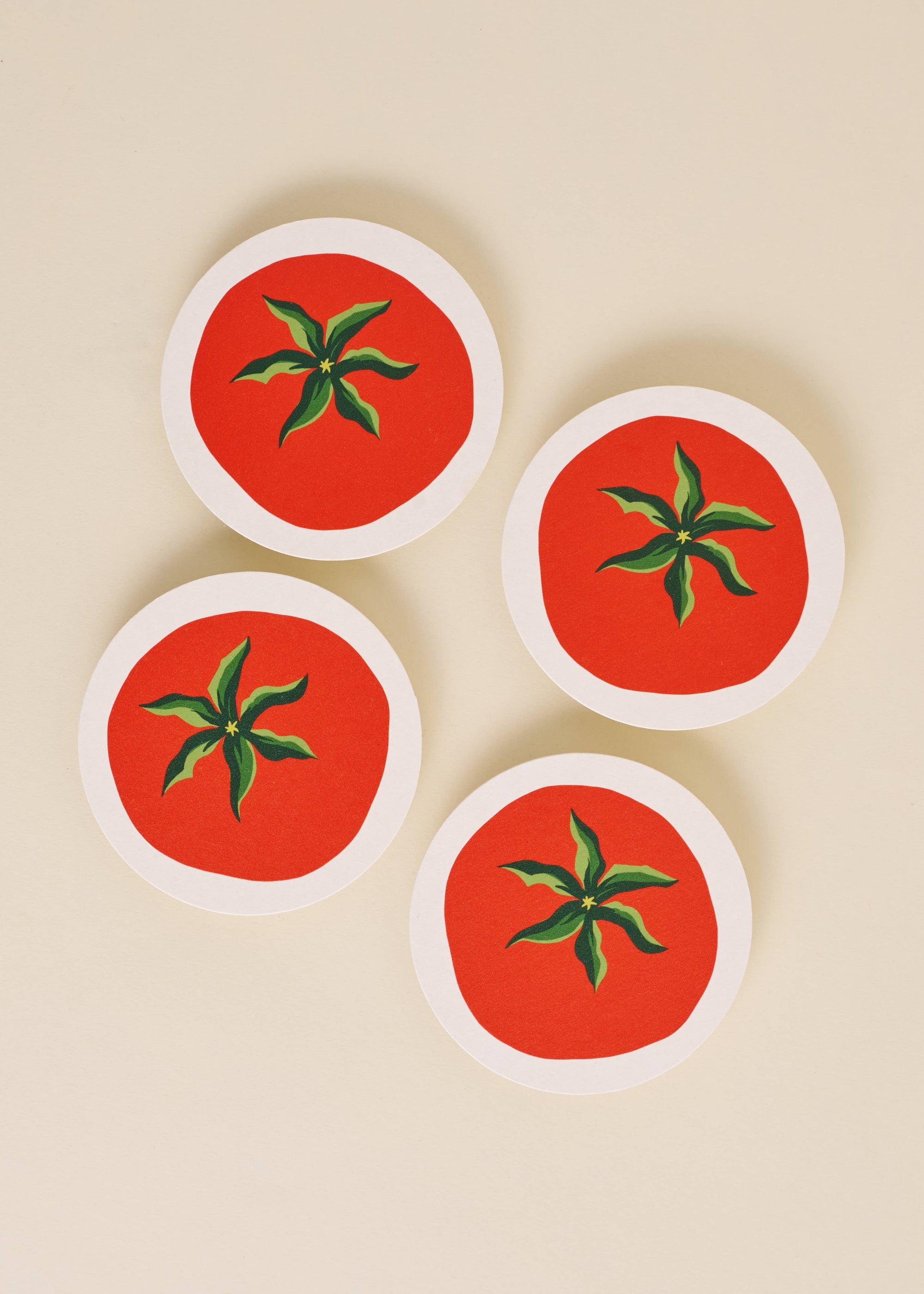 Four round coasters with tomato design on a beige background