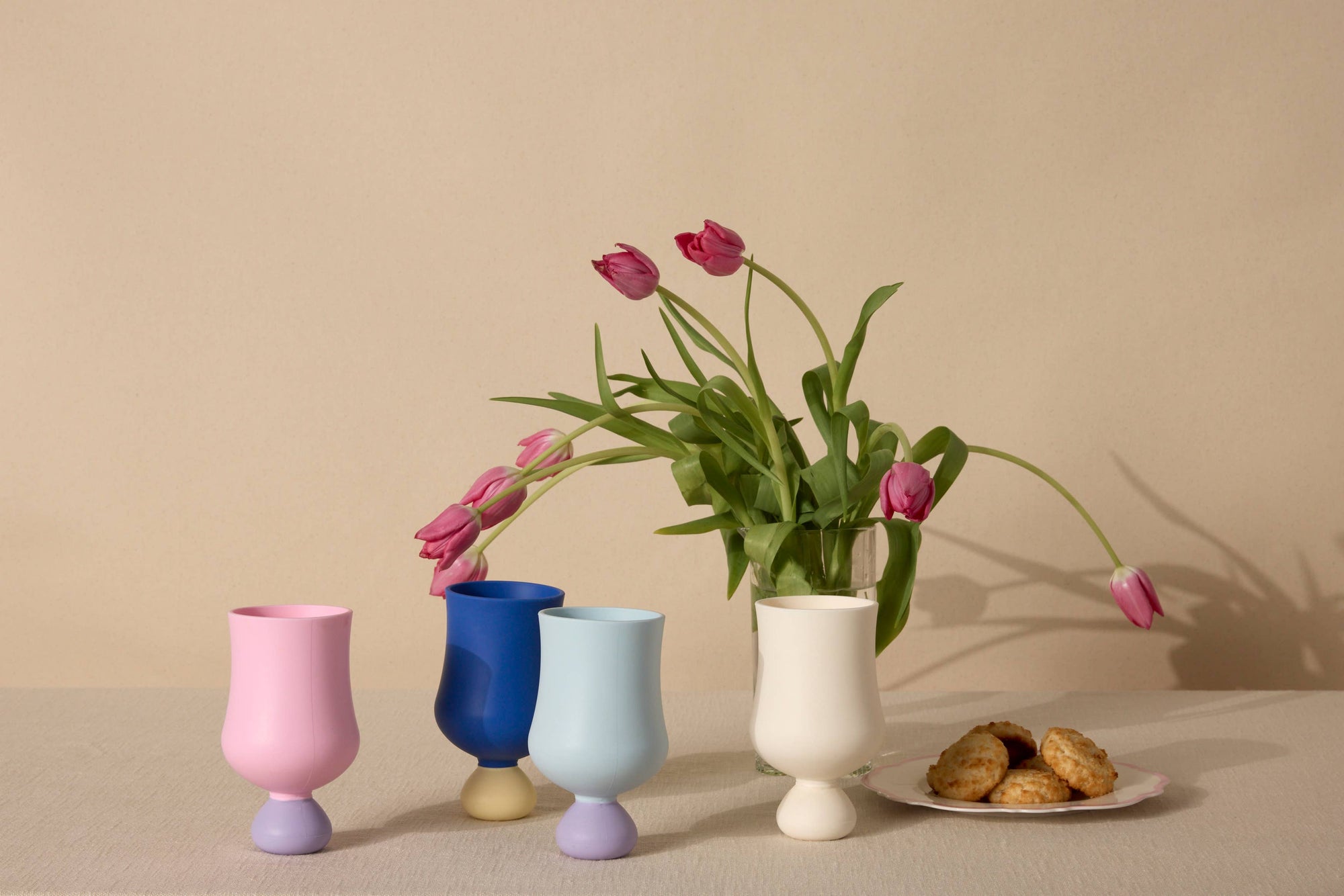 Set of colorful silicone cups with tulips and cookies on a beige background