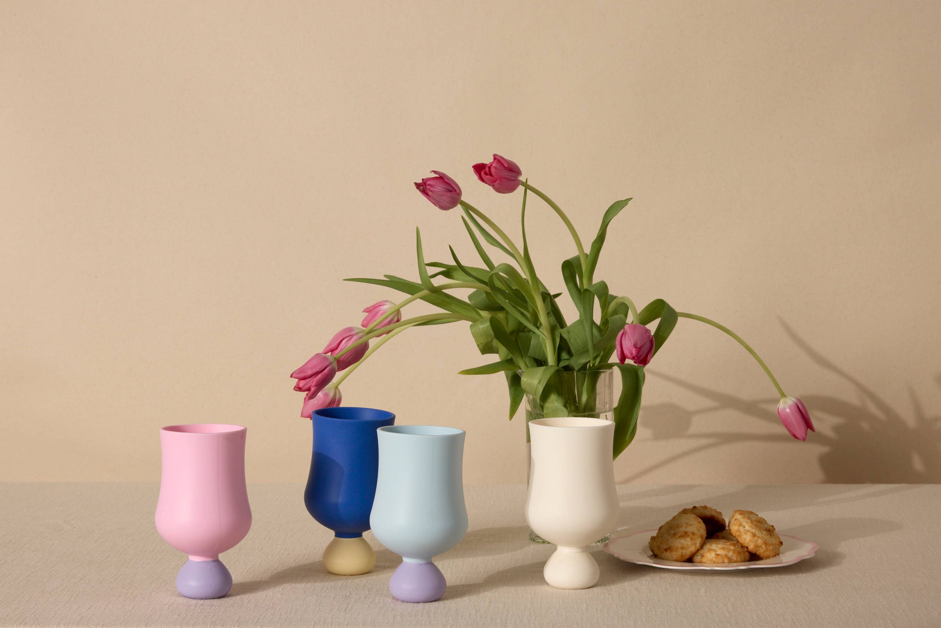 Set of colorful silicone cups with tulips and cookies on a beige background