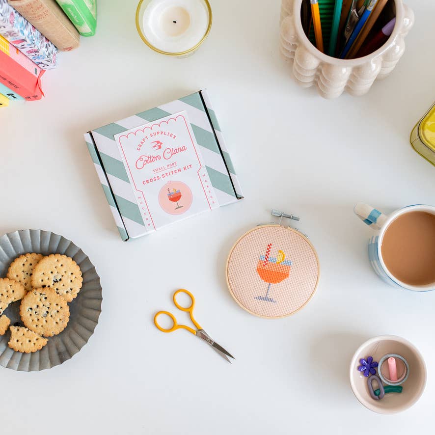 Crafting supplies including a book, scissors, cookies, and a cup on a white surface.
