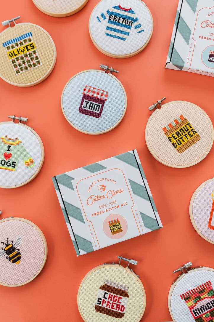 Collection of cross-stitched embroidery hoops on an orange background with a Cotton Clara box.