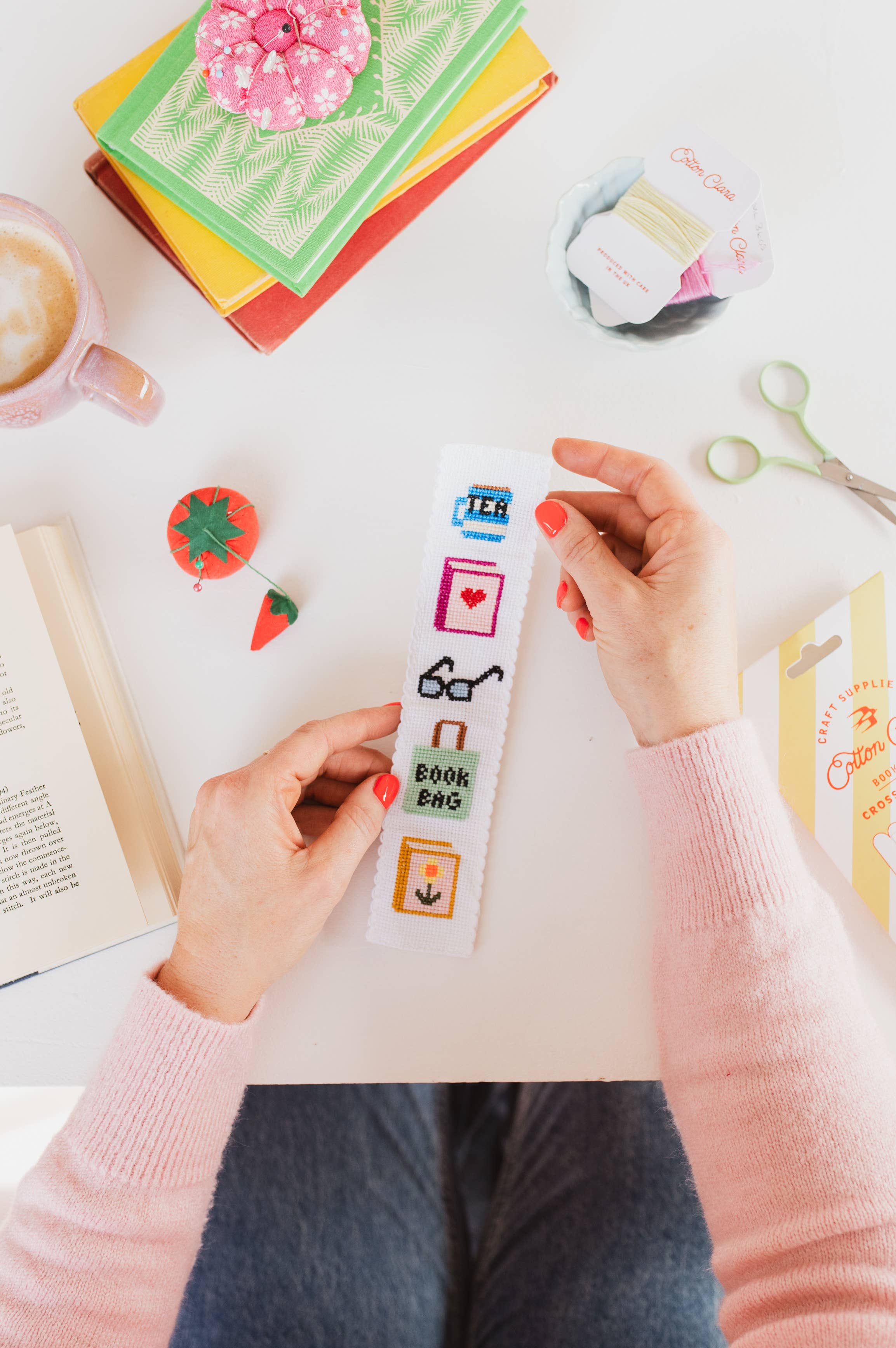 Person holding a colorful bookmark with icons on a desk with stationery items.
