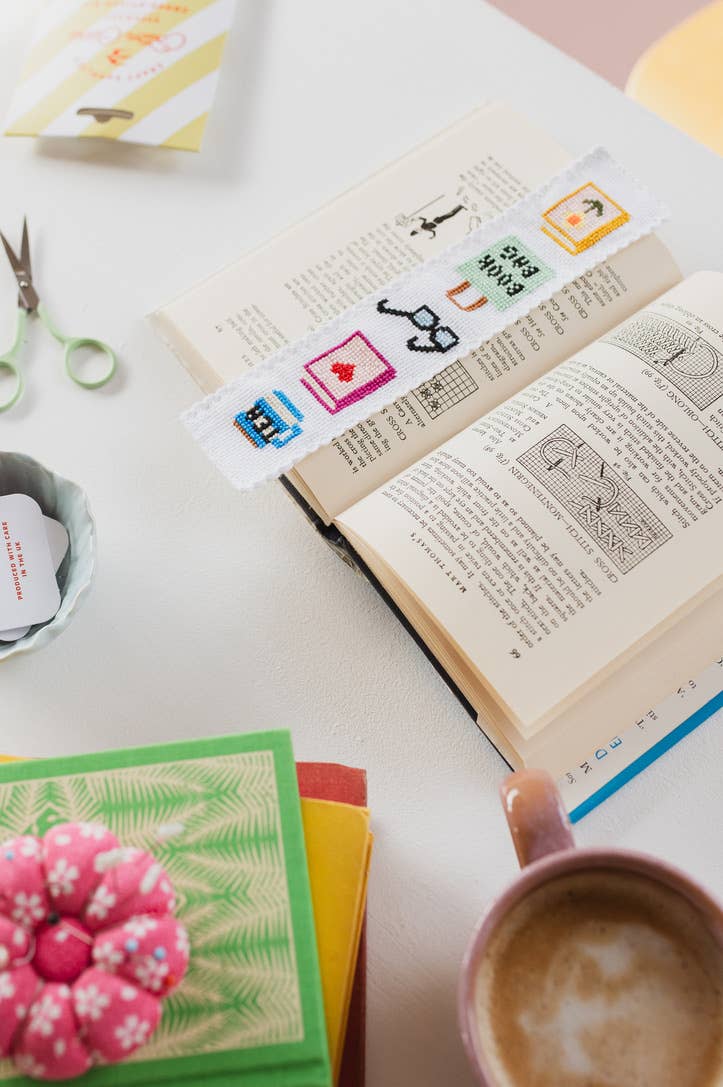 Open book with colorful bookmarks on a table with a mug and stationery items.