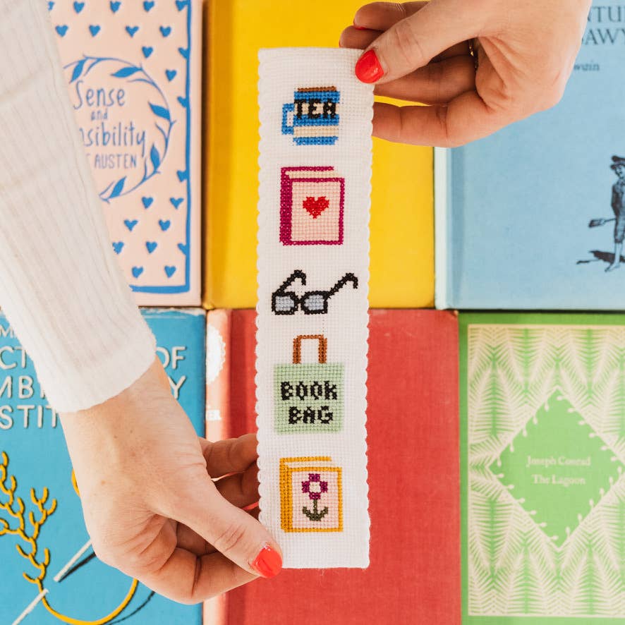 Cross-stitched bookmark held over a stack of colorful books