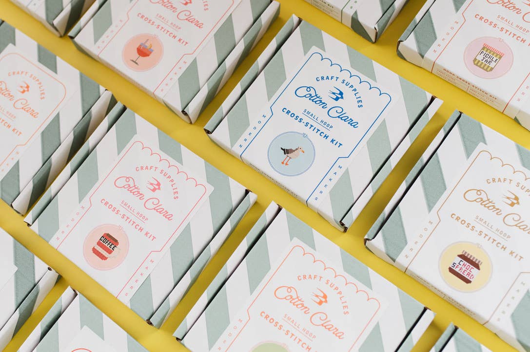 Close-up of 'Cotton Club' craft stitch kit boxes arranged on a yellow metal rack.