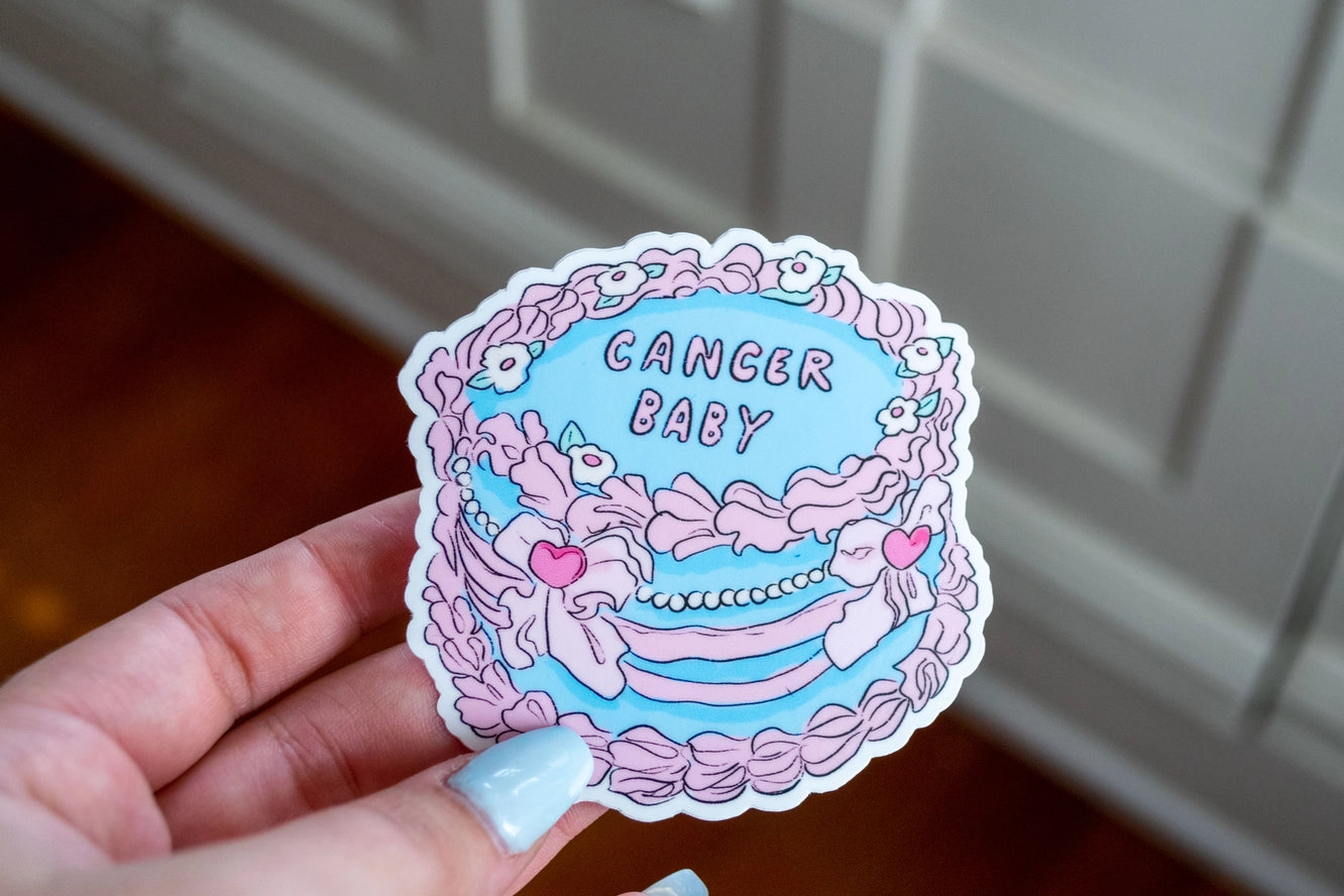 Sticker with 'Cancer Baby' text held by a hand against a neutral background