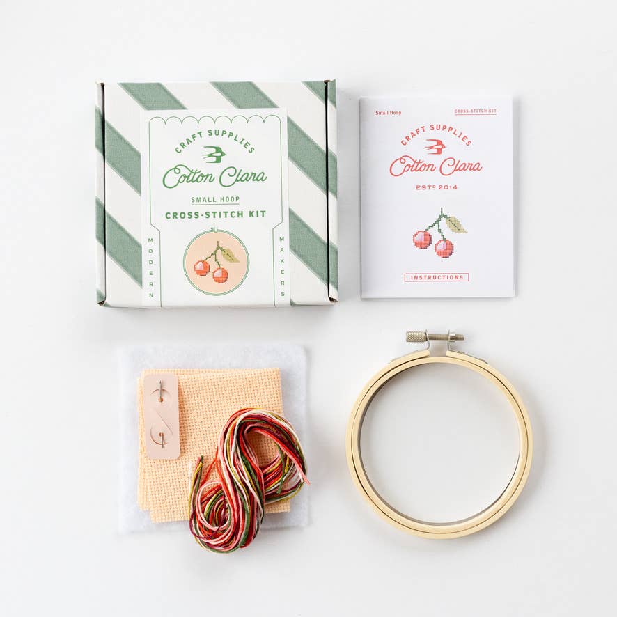 Cross-stitch kit with hoop, thread, and packaging on a white background
