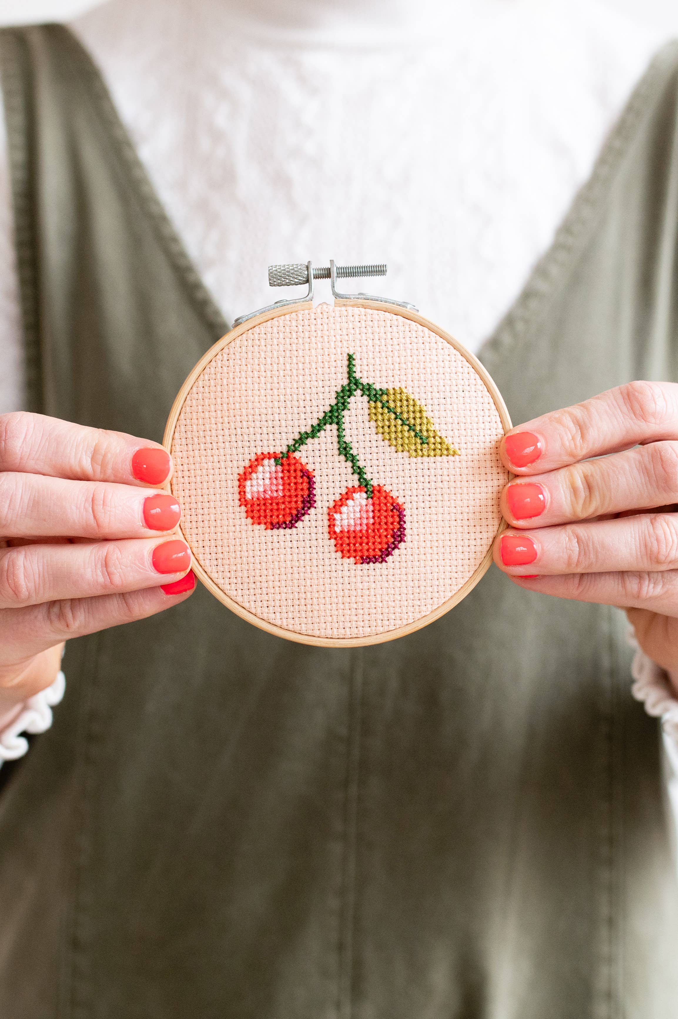 Embroidery hoop with cherry design held by hands against a neutral background