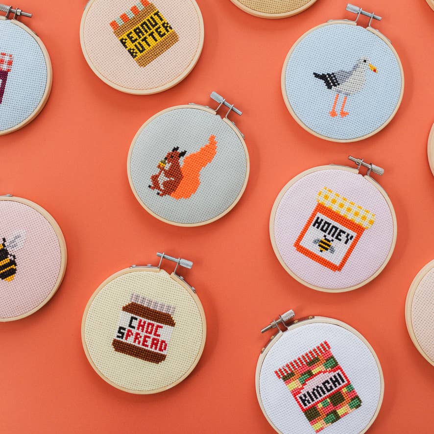 Collection of cross-stitched hoops with various designs on an orange background