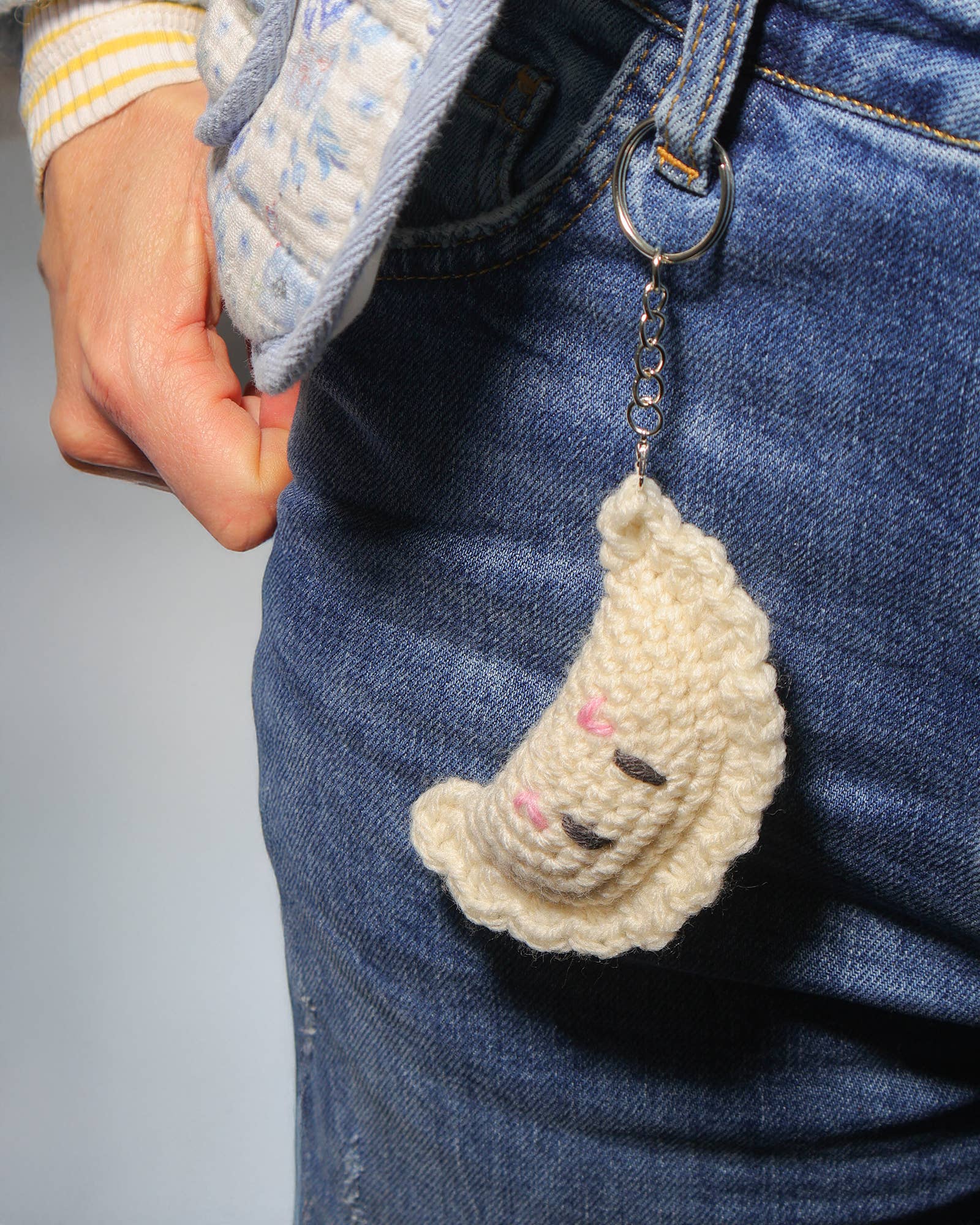 Handmade crochet keychain shaped like a cloud with a face attached to blue jeans.