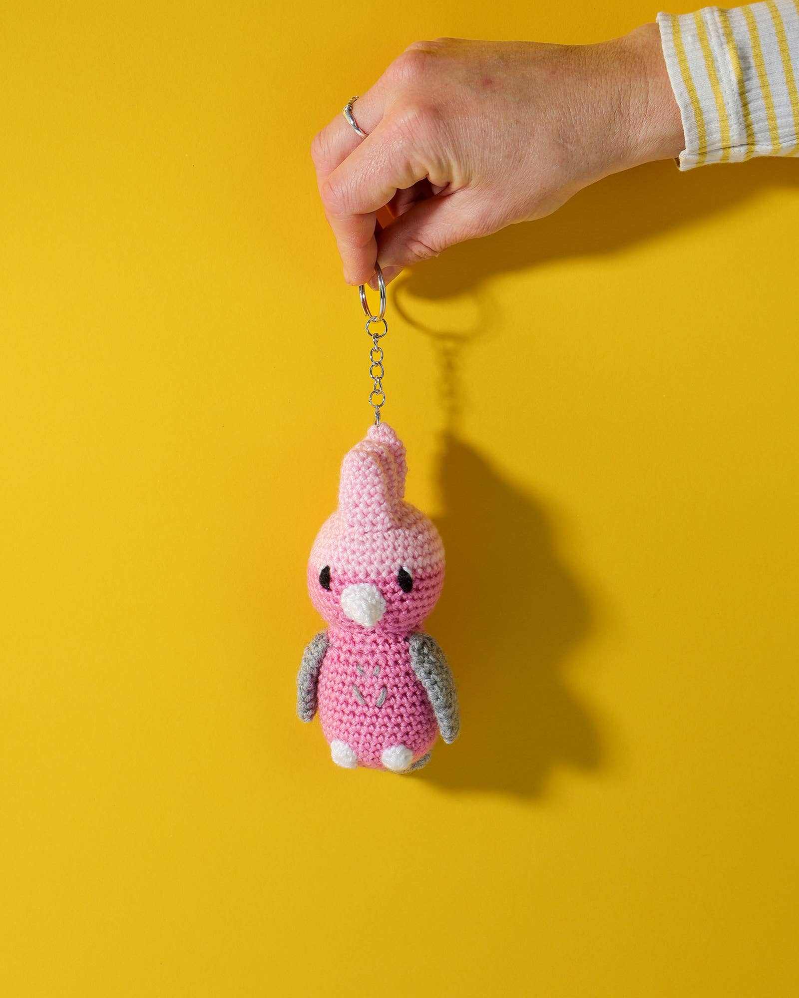 Pink crochet keychain held by a hand against a yellow background