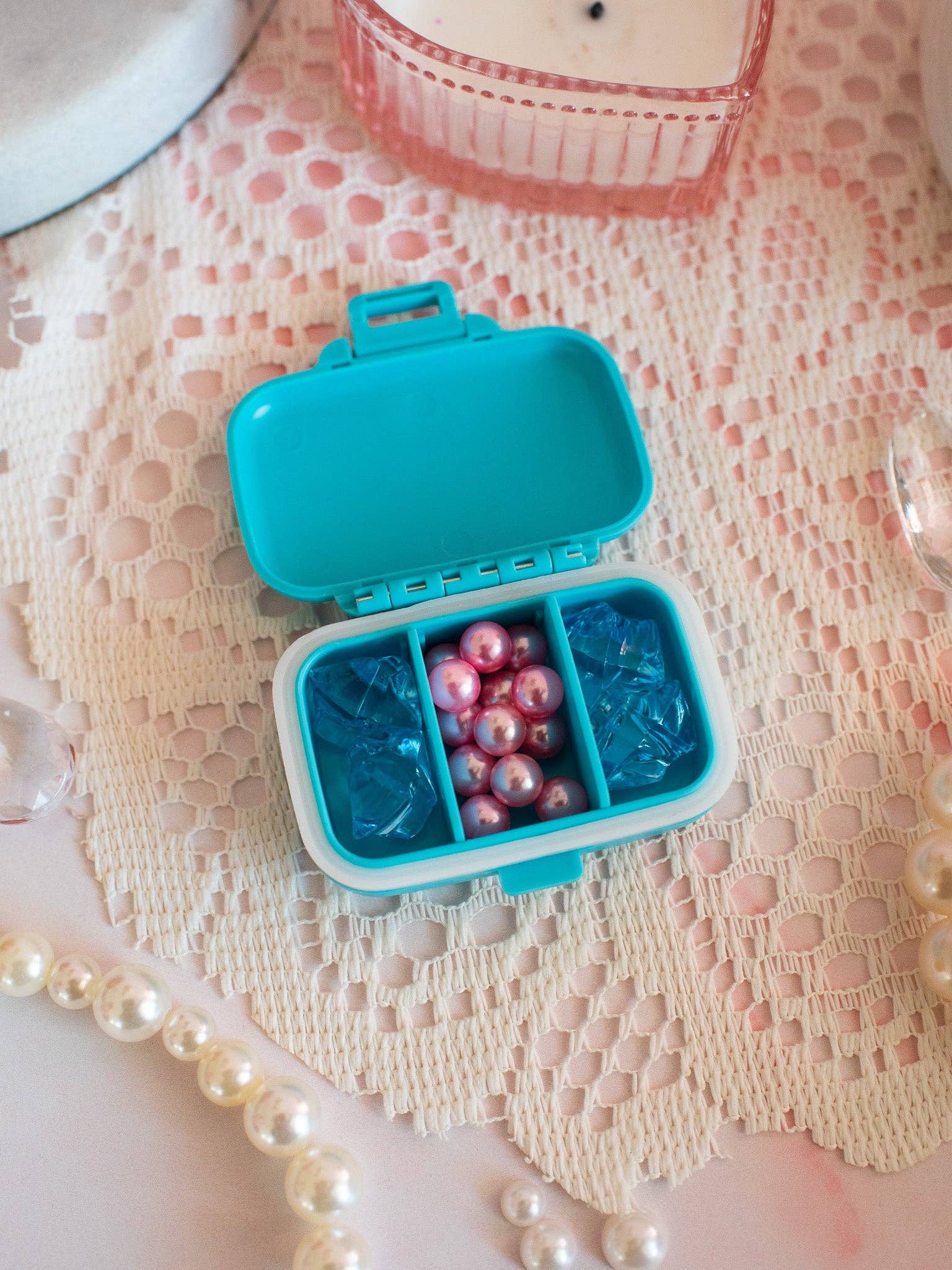 Blue pill organizer with pearls and blue gummy bears on a textured surface