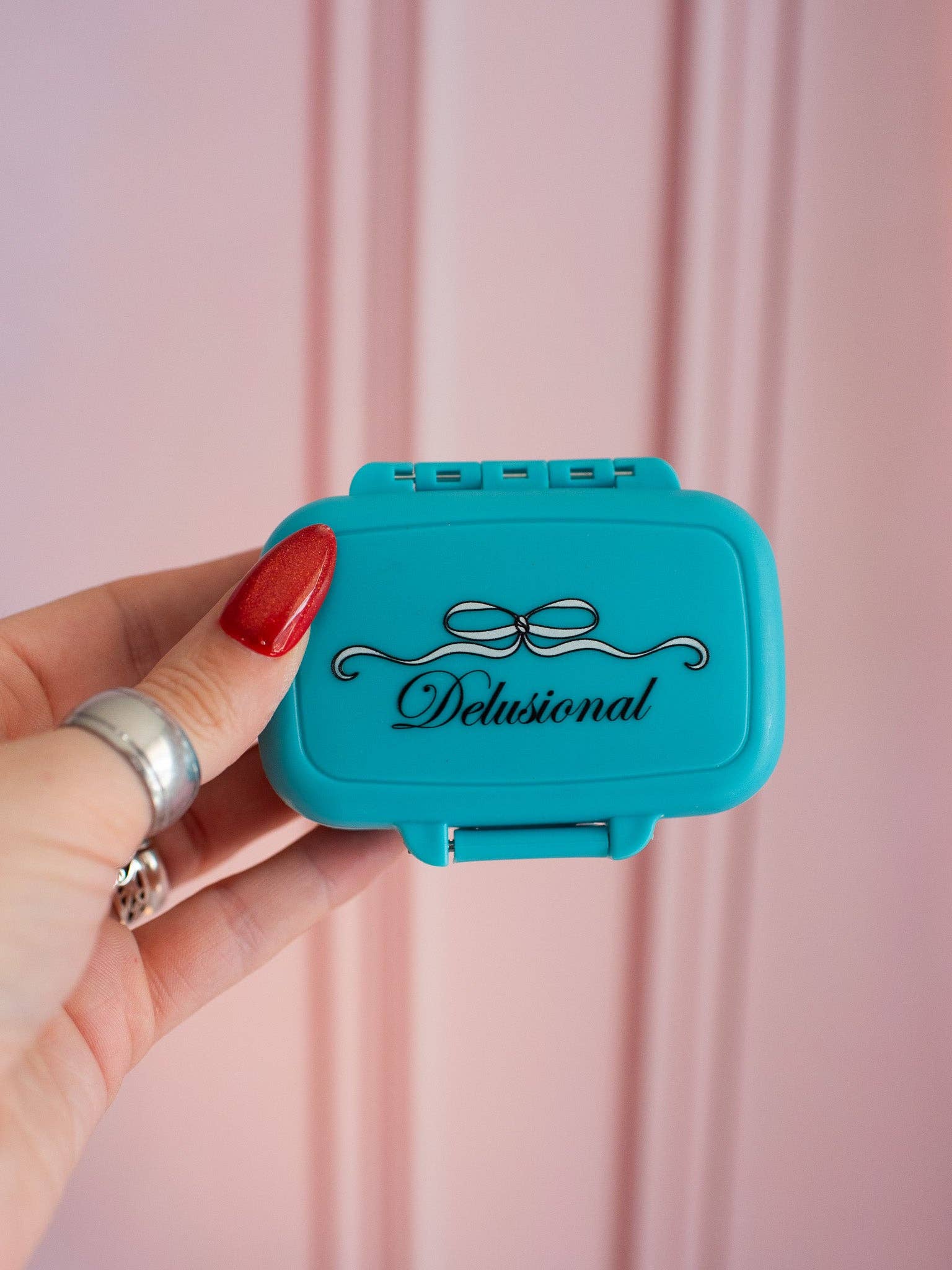 Turquoise case with 'Delusional' branding held by a hand against a pink background