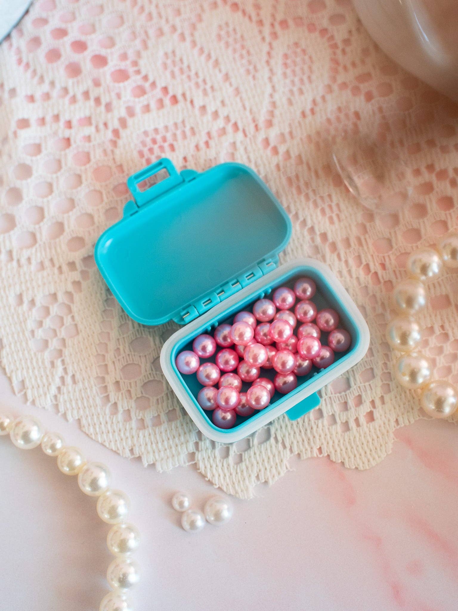 Blue container filled with pink pearls on a lace background