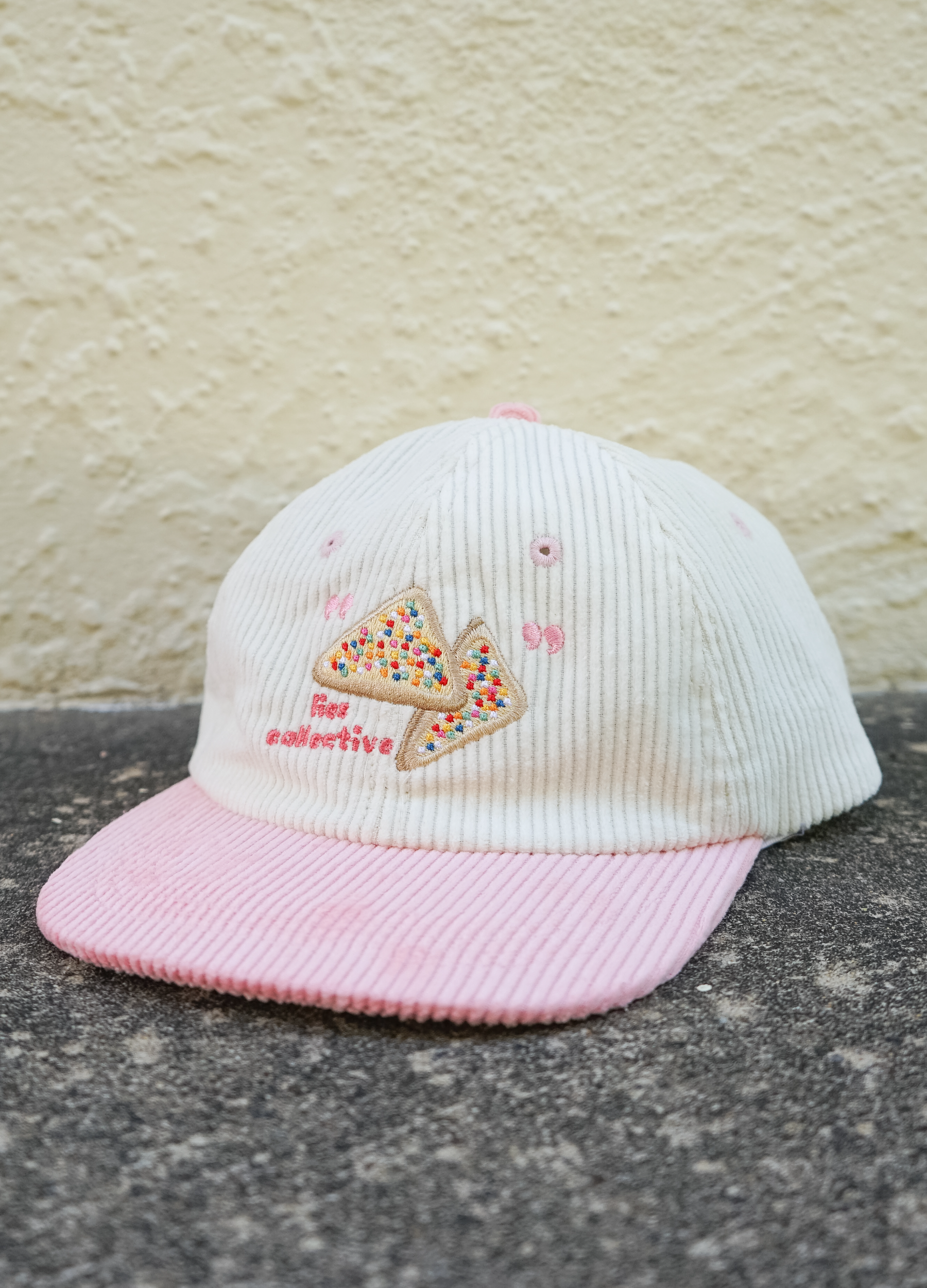 White and pink cap with embroidered design on a textured surface
