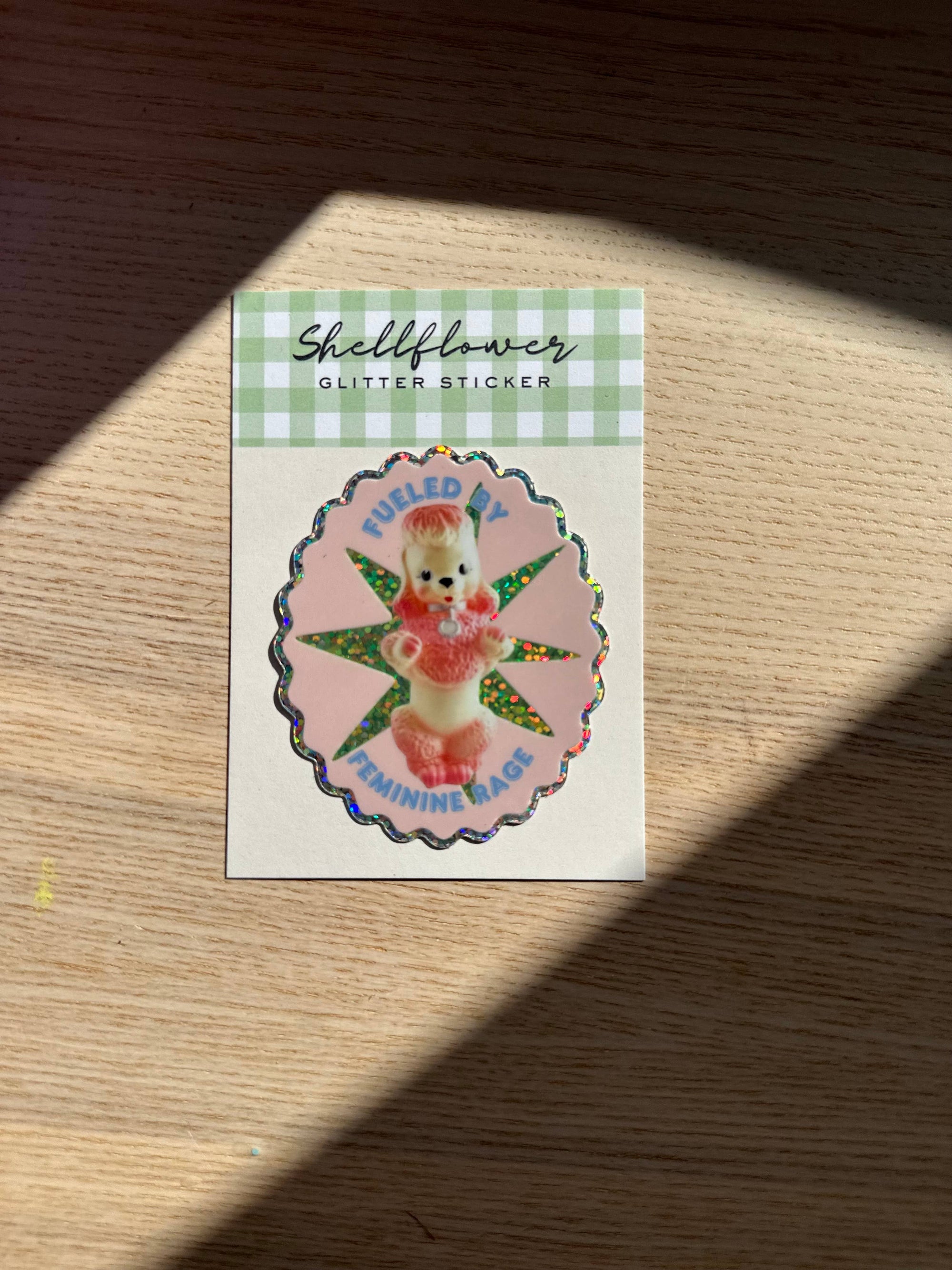 Sticker with a character design on a checkered background, placed on a wooden surface.