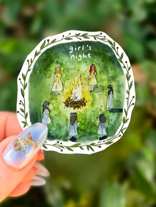 Decorative plate with illustration of 'girl's night' and people around a campfire, held against a green leafy background.