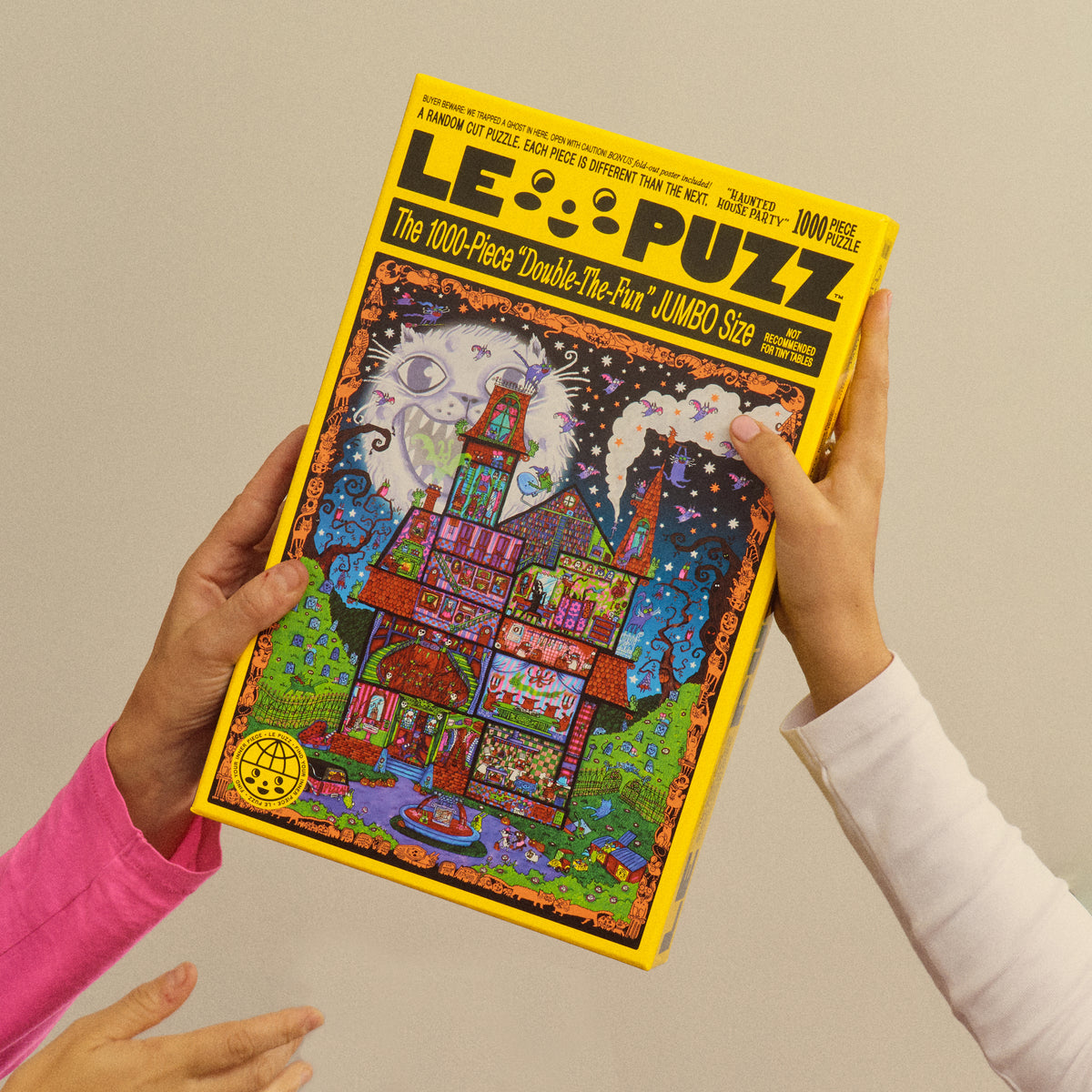 Two people holding the yellow Le Puzz Haunted House Party 1000-piece puzzle box.