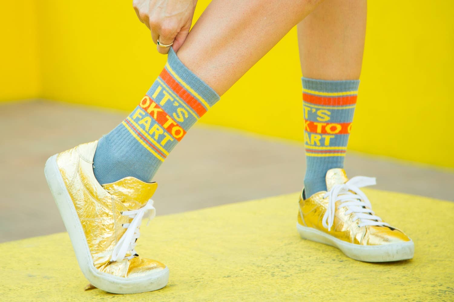 Person wearing colorful socks with text and yellow sneakers on a yellow background