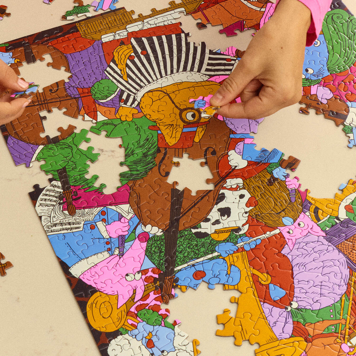 Close-up of hands assembling the Le Puzz K9 Symphony puzzle, featuring colourful dogs playing orchestral instruments