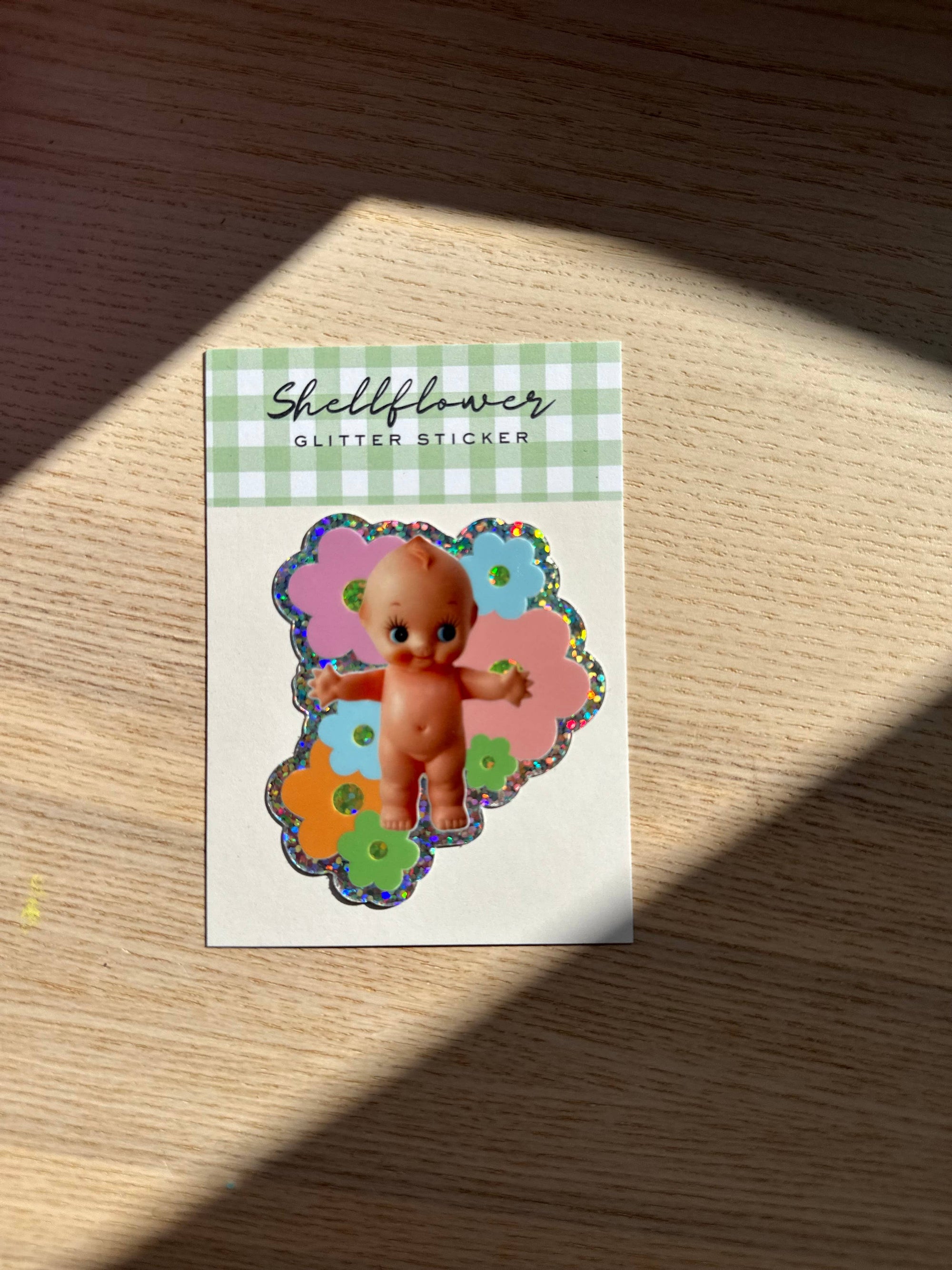 Sticker with a baby doll design on a checkered background, placed on a wooden surface.
