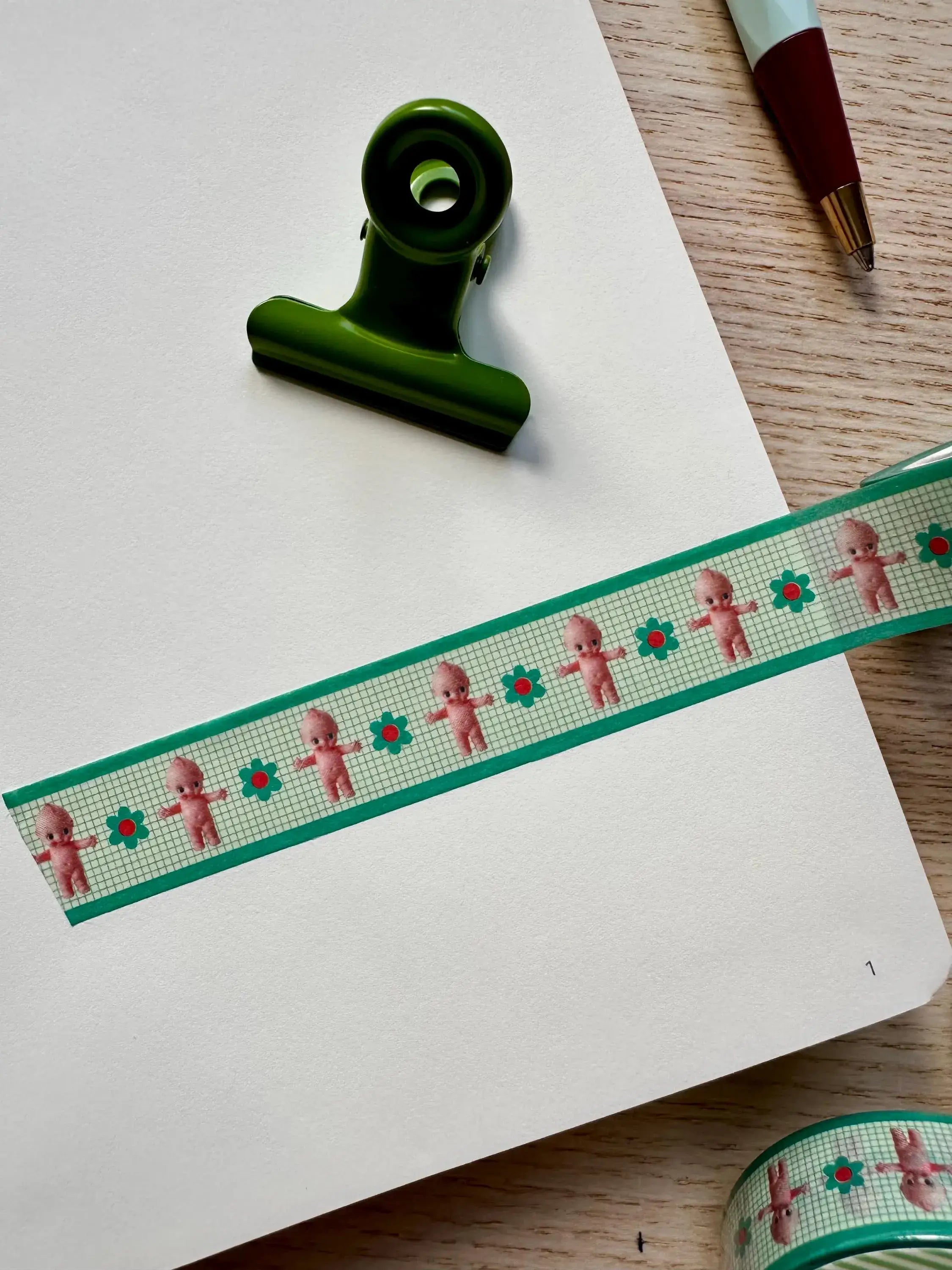 Decorative ribbon with teddy bear pattern on a notebook with a green clip.