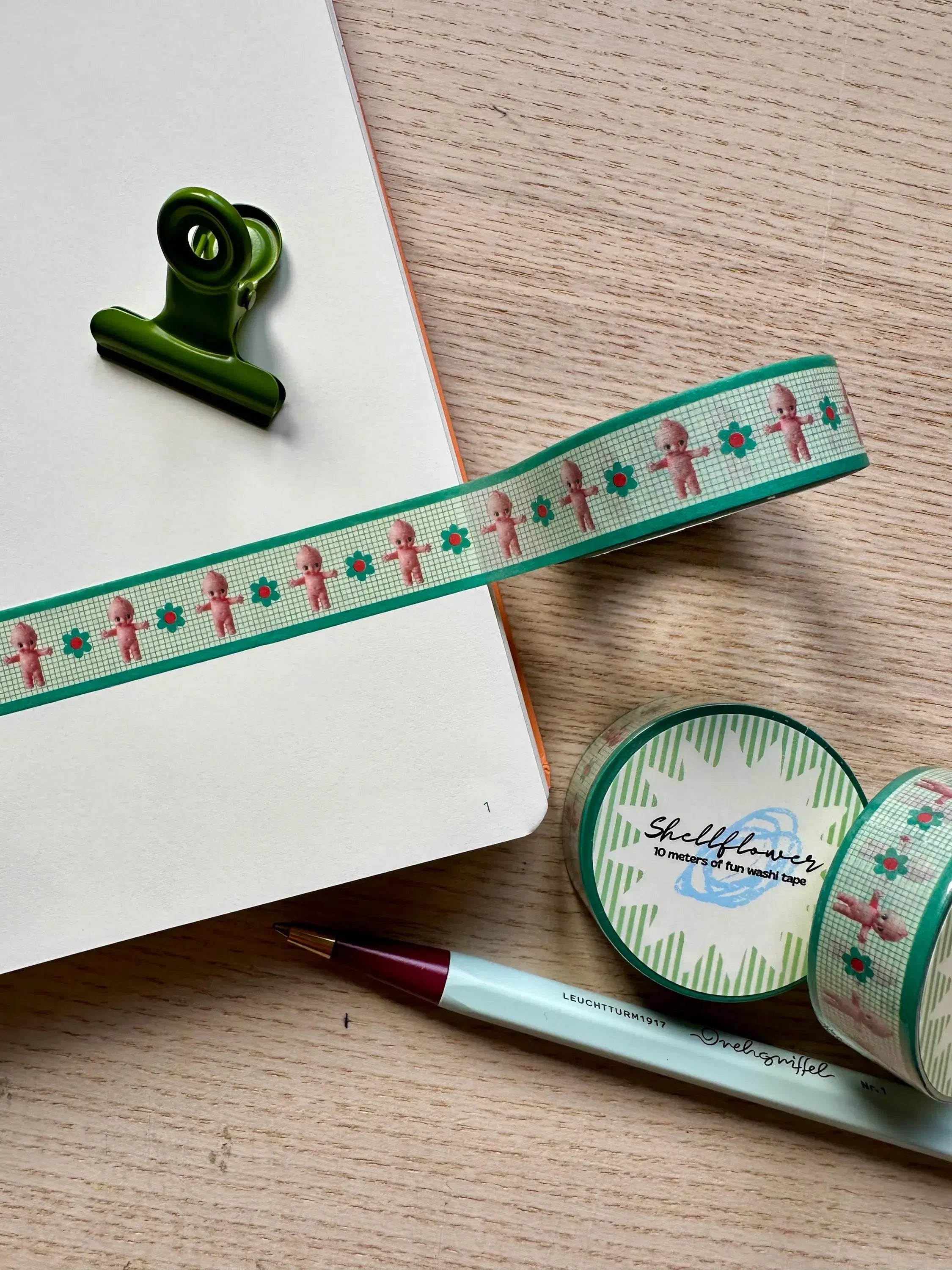 Decorative ribbon with gingerbread men design on a wooden surface with a pen and paper clip.