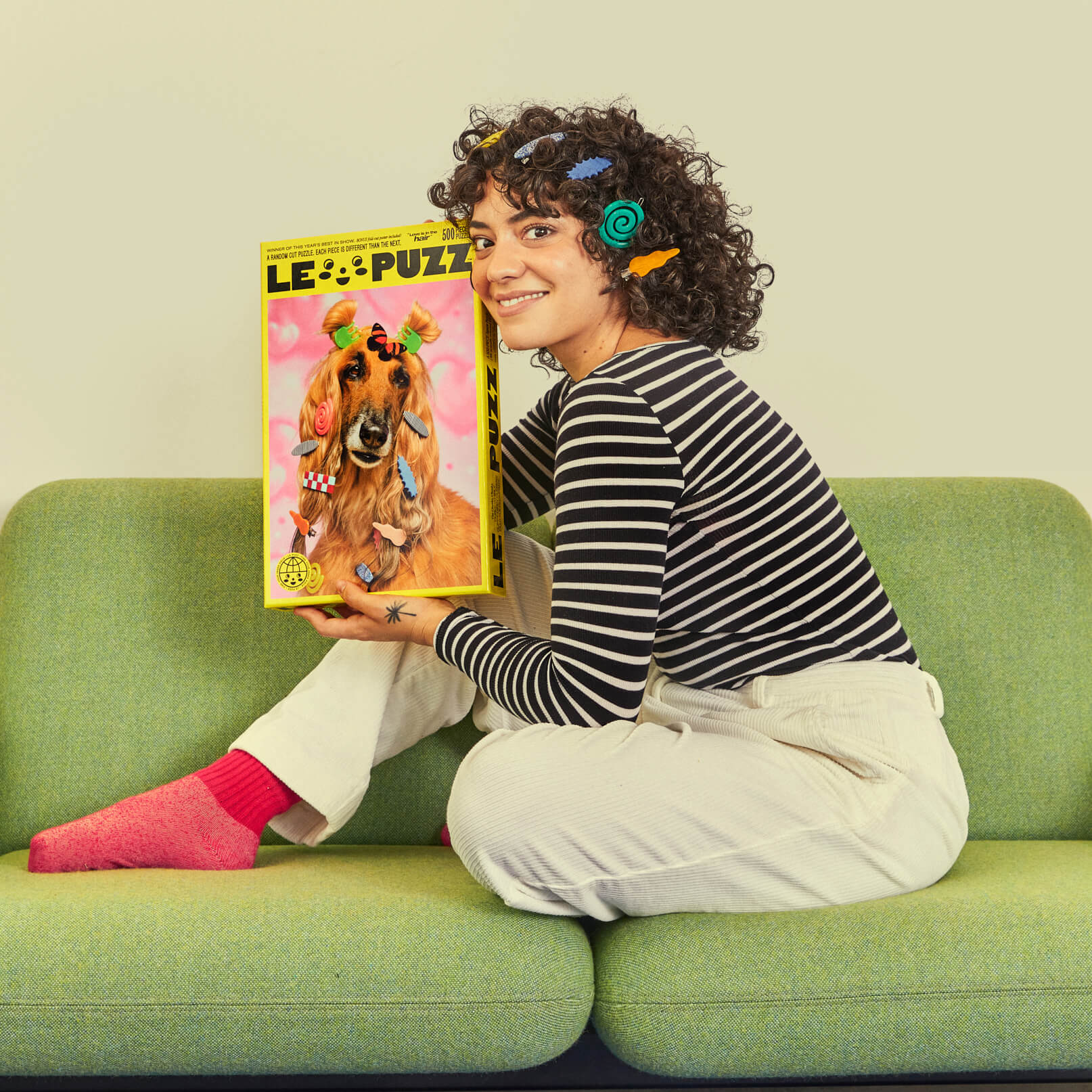 Person holding a puzzle box with a dog on it, sitting on a green couch.