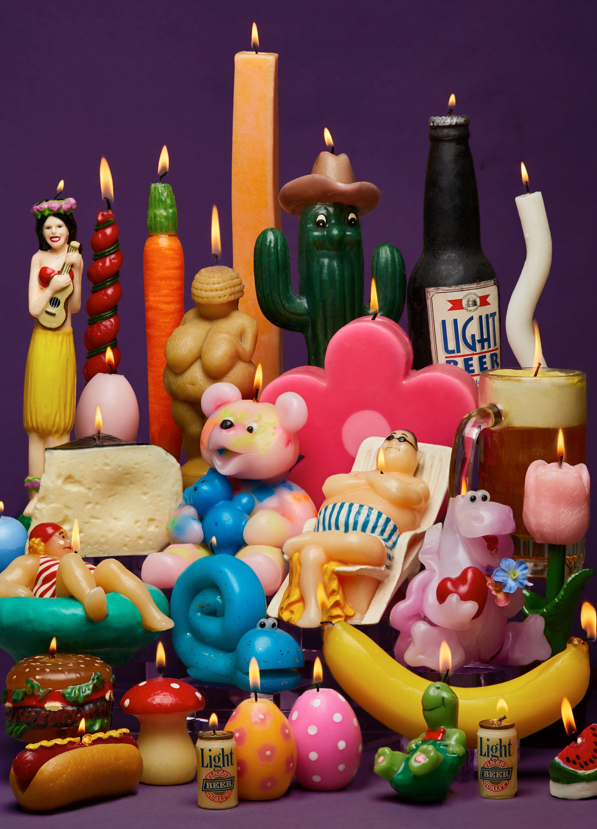Colorful assortment of novelty candles and beer bottles on a purple background