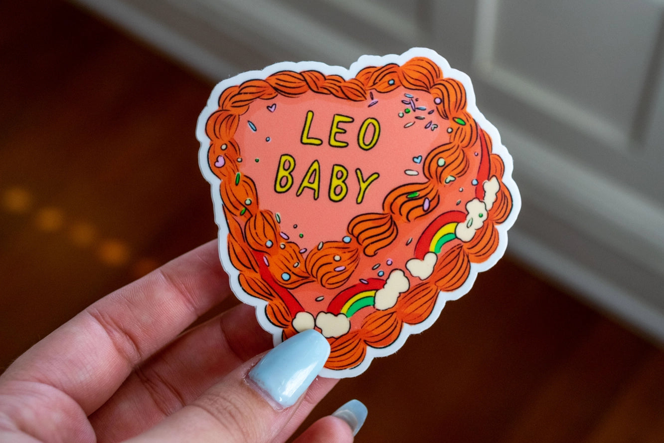 Sticker with 'Leo Baby' text held by a hand with light blue nail polish.