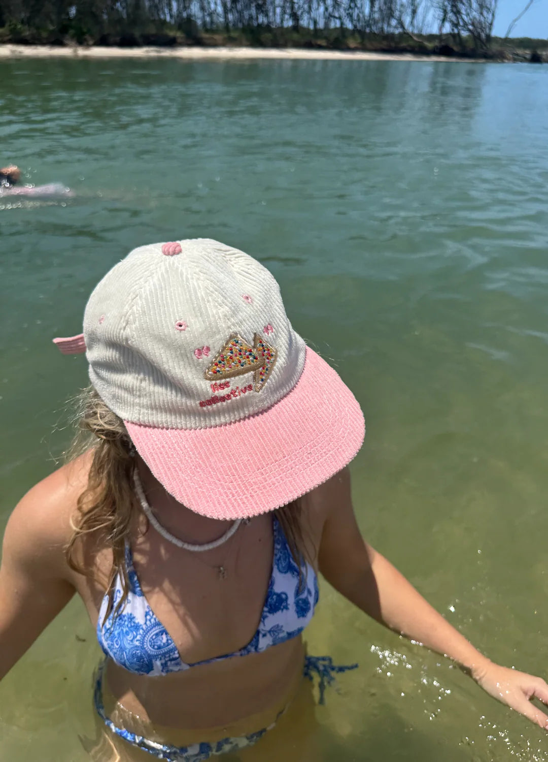 Person wearing a pink and white cap and blue bikini in shallow water.