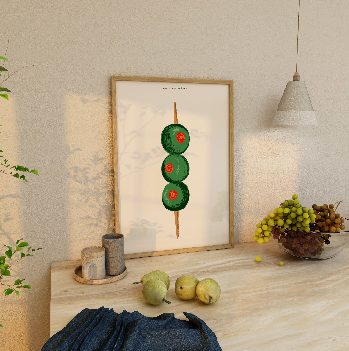 A framed print of a stylized martini olive on a wooden surface, with a glass of water and some fruits in the background.