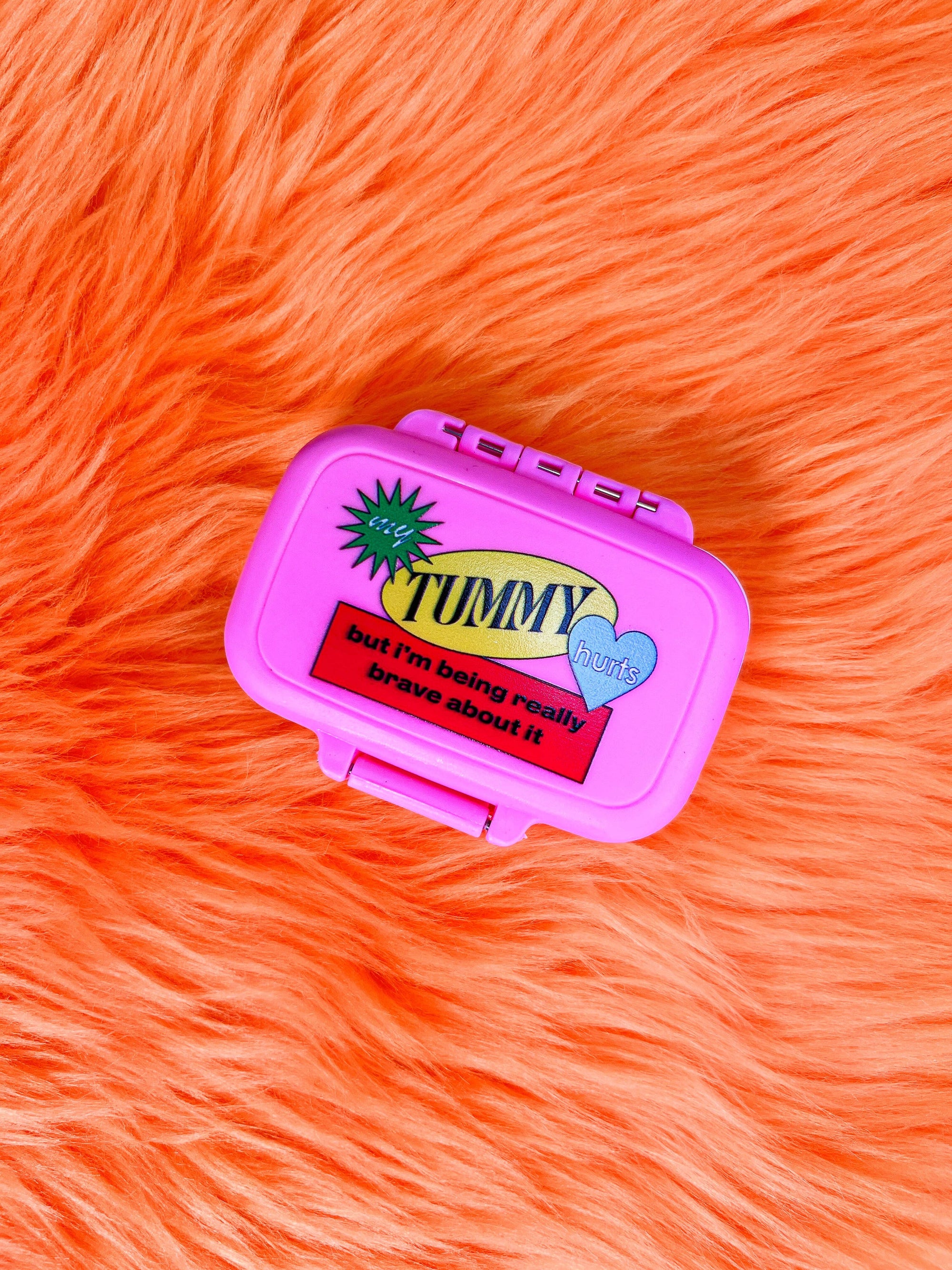 Pink pill case with text on an orange fur background